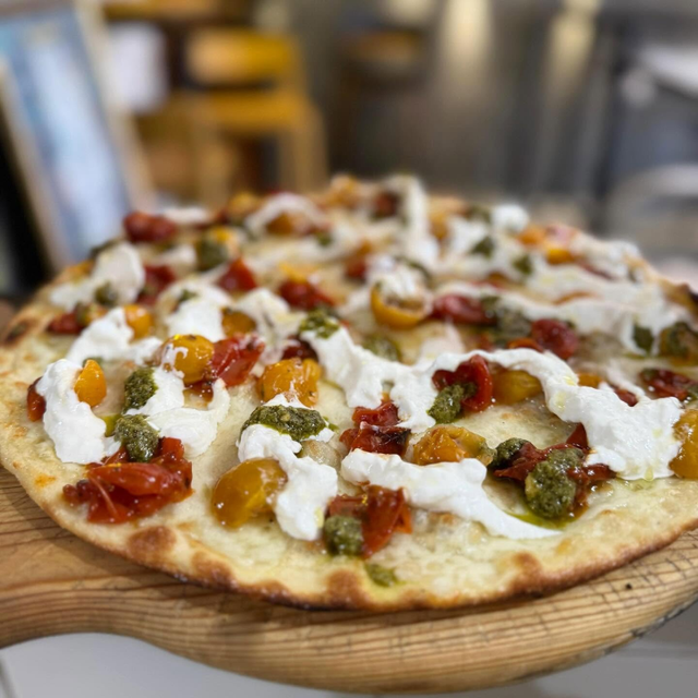 Pizza con pomodori, formaggio ed erbe aromatiche, servita su un tagliere di legno