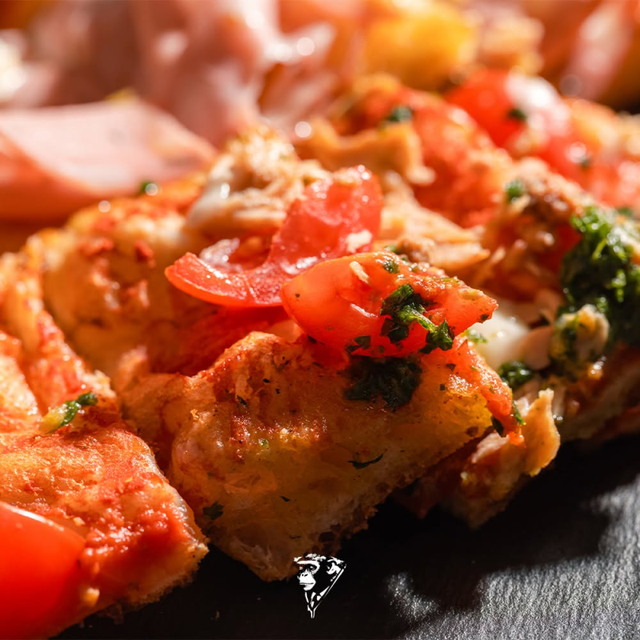 Primo piano di patate arrosto croccanti, guarnite con pomodori a dadini ed erbe aromatiche, su un piatto nero