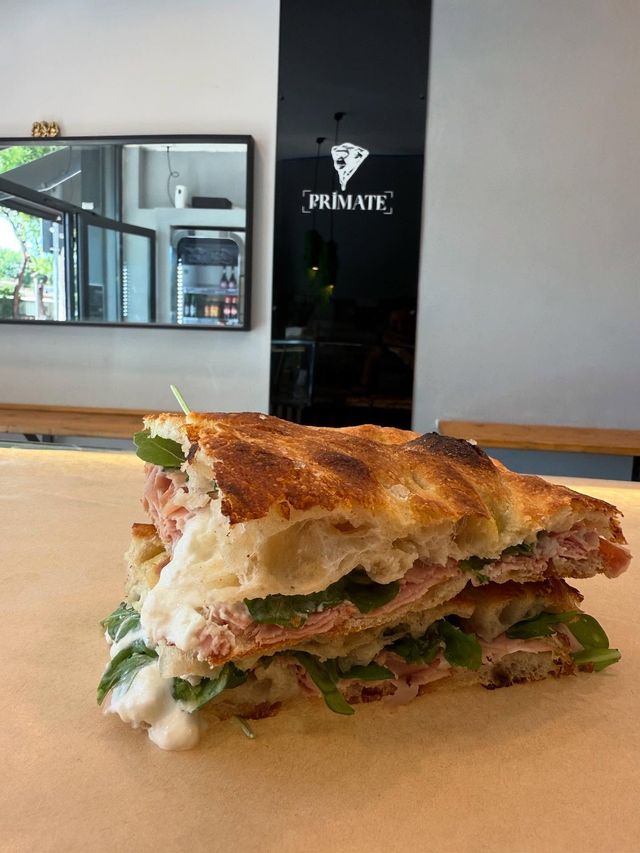 Un panino morsicato su carta marrone in un bar, con una parete nera e uno specchio sullo sfondo.