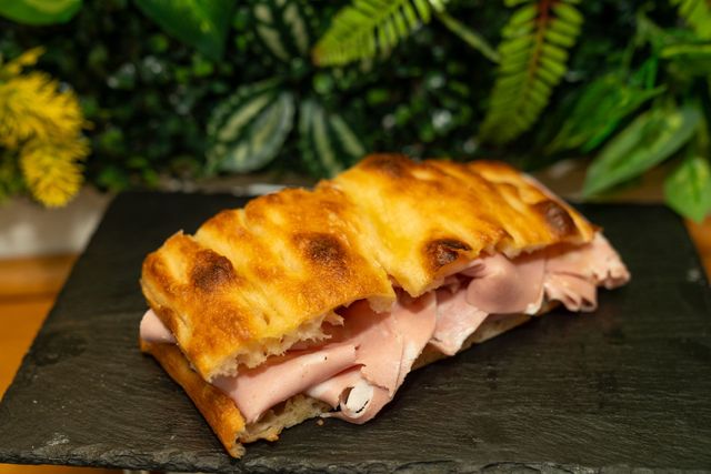 Panino grigliato con carne affettata su un tagliere di ardesia nera, guarnito con verdure sullo sfondo