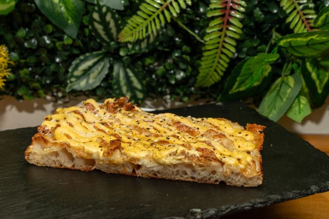 Una fetta di focaccia al forno filante su un piatto di ardesia scura, con foglie verdi di felce sullo sfondo