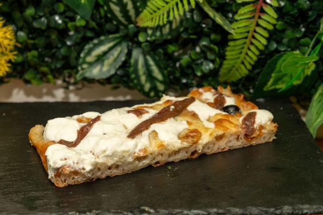 Fetta di pizza dolce con copertura bianca fusa e cioccolato colato sopra, su una lastra di ardesia scura