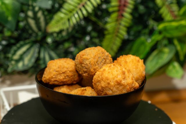 Ciotola di snack dorati e fritti su un tavolo, con del fogliame verde sullo sfondo