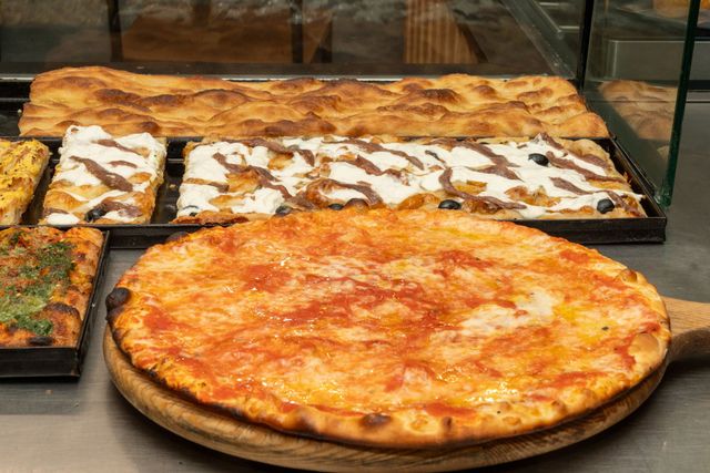 Esposizione in pizzeria con una grande pizza al formaggio e fette di pizza rettangolari