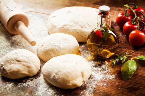 Palline di impasto su un tavolo di legno infarinato con un mattarello, olio d'oliva, pomodori e basilico.