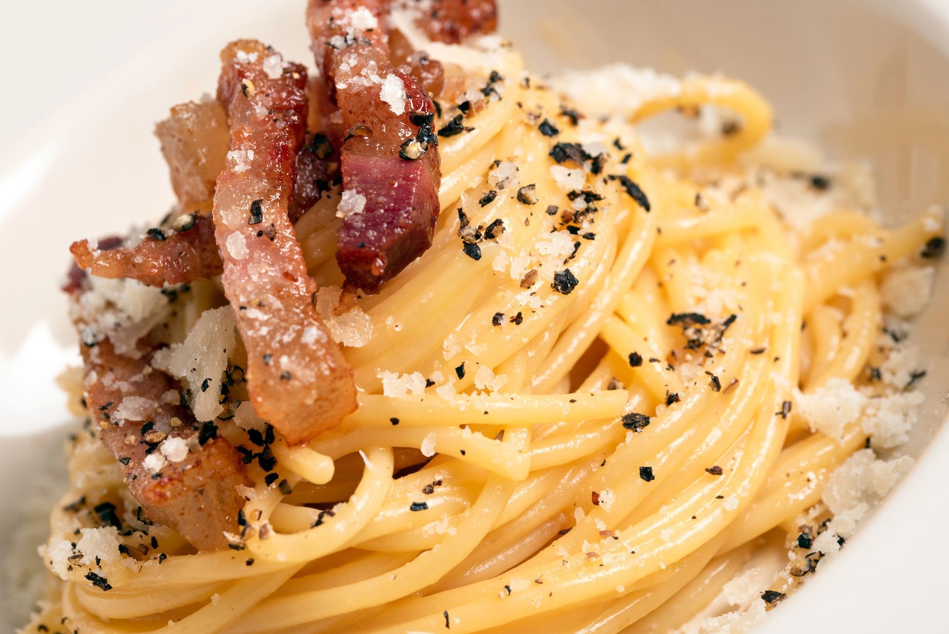 Spaghetti alla carbonara con pancetta, pepe nero e formaggio grattugiato, serviti su un piatto bianco