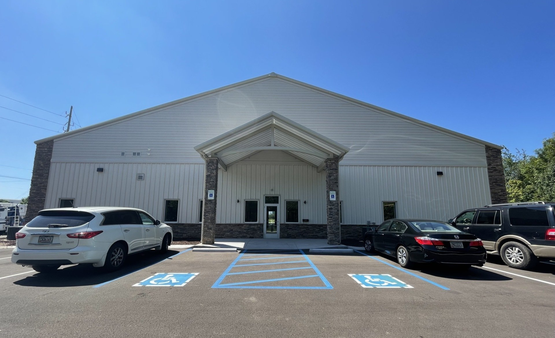 Exterior of a large, white metal building with stone accents. Accessible parking spaces in foreground.