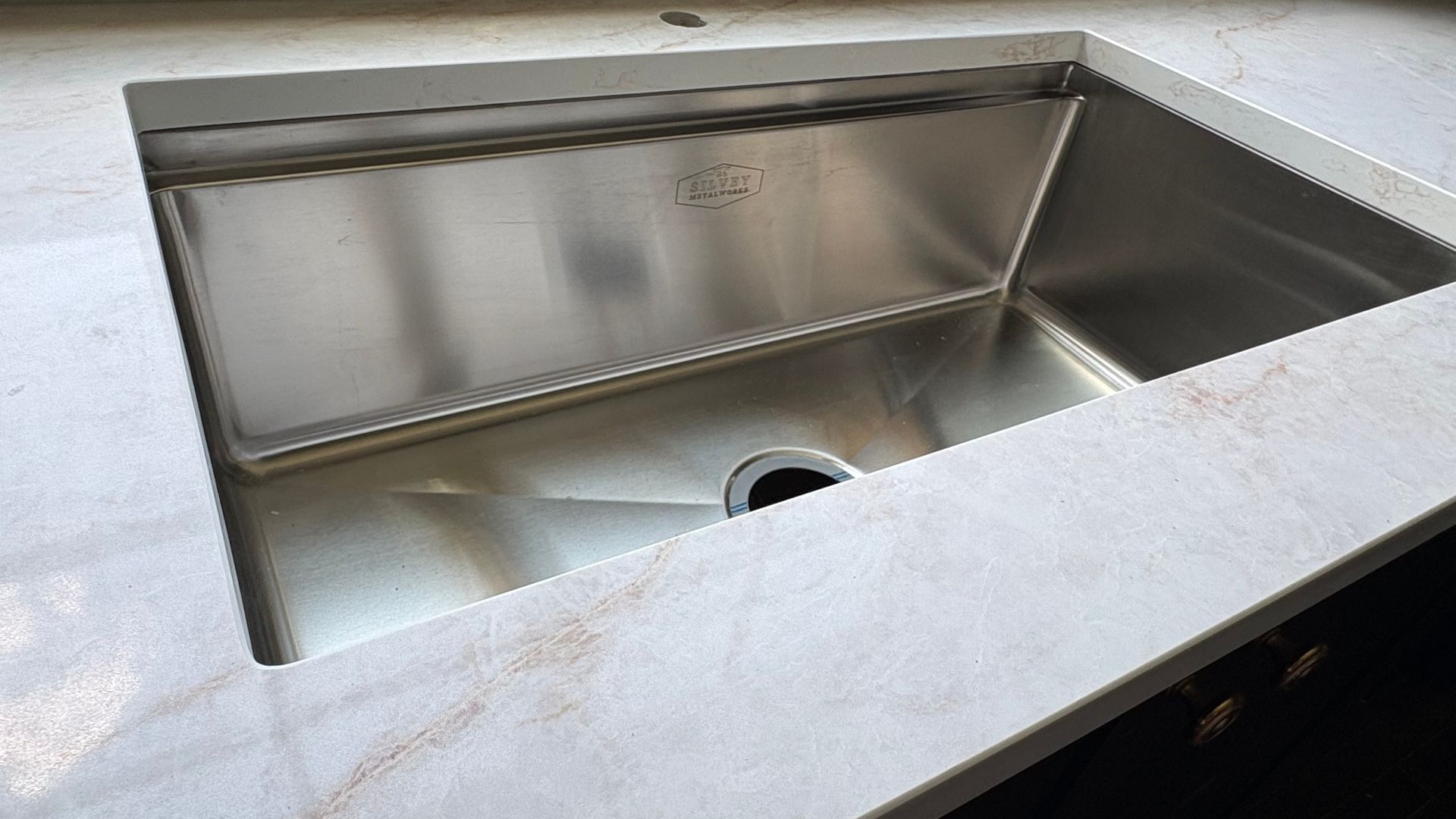 Stainless steel kitchen sink with single basin and drain opening, set in a light countertop.