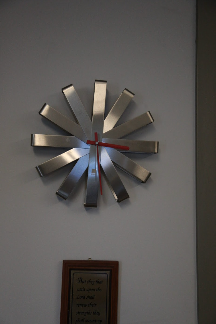 A stainless steel clock with a red hands on a white wall