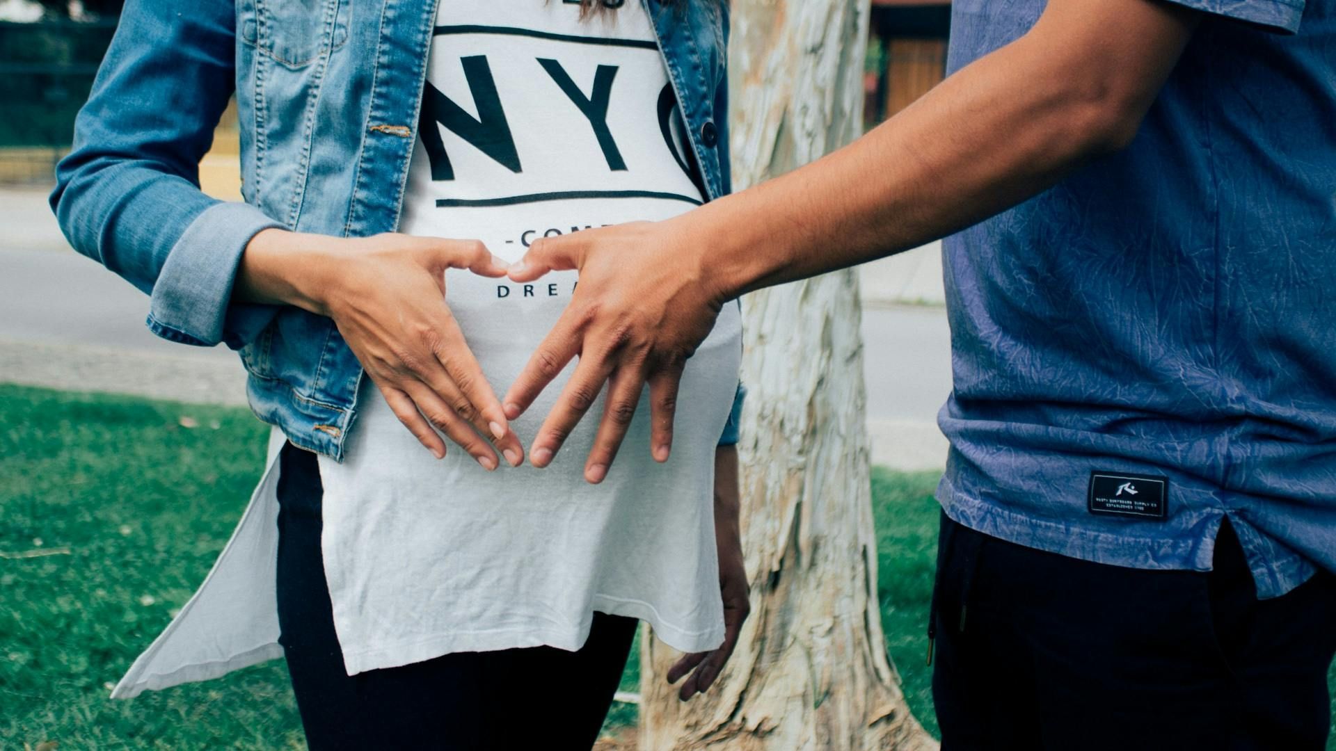 A pregnant woman and her partner make a heart shape with their hands over the baby