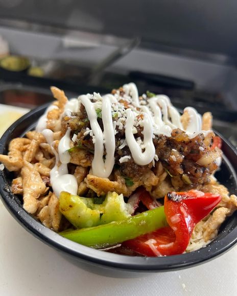 A close up of a bowl of food with chicken and vegetables on a table.