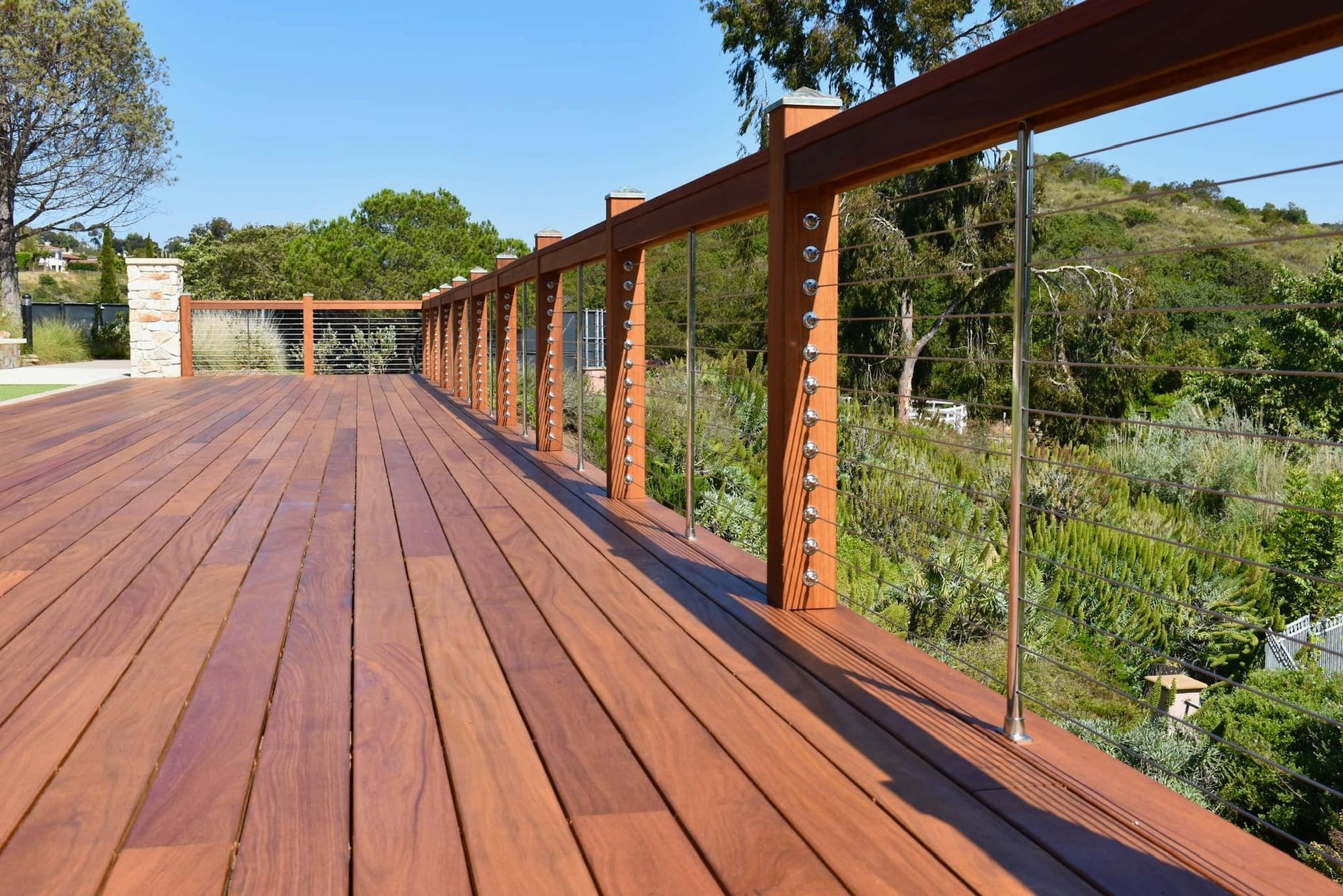 Wooden deck walkway with railings overlooking lush greenery under a clear blue sky