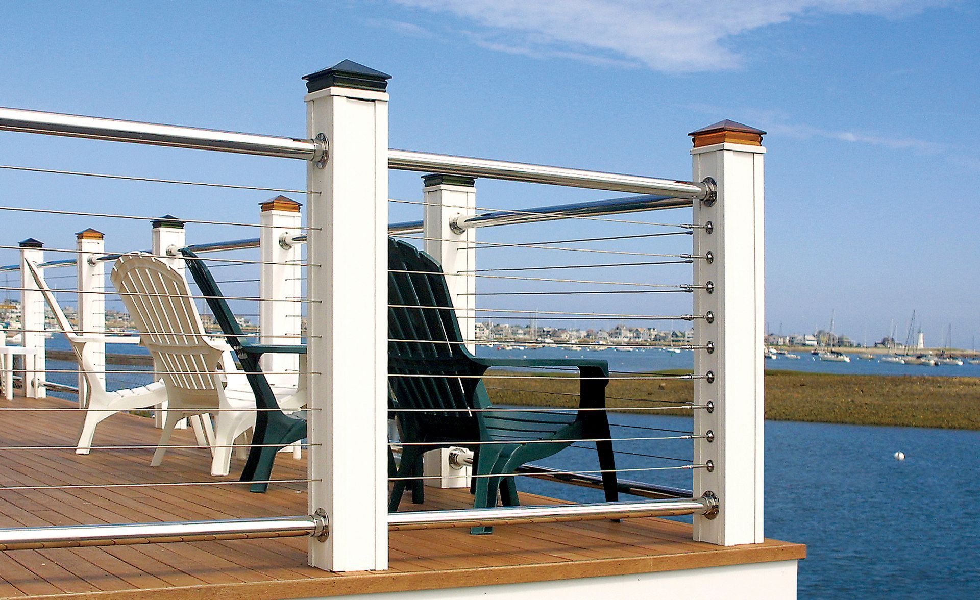 Deck chairs by a waterfront railing overlooking calm blue water and a distant shoreline