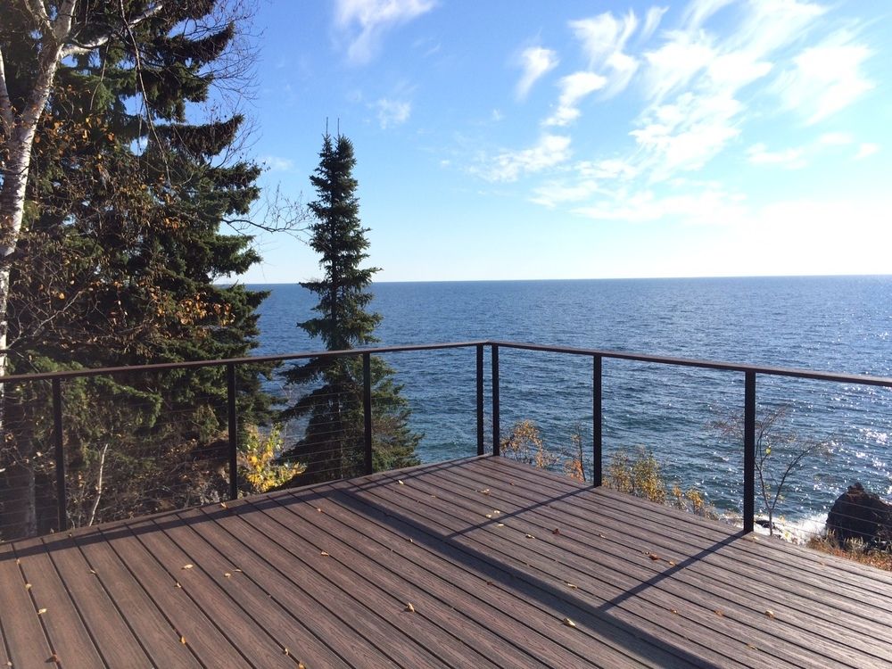 Deck overlooking a blue lake with pine trees and a bright sky