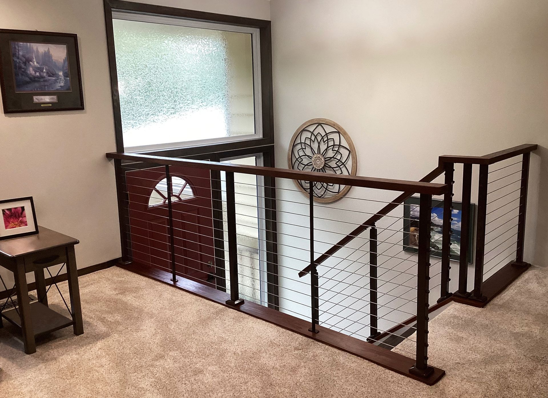 Indoor stair landing with dark wood railing, frosted window, and beige carpeted hallway.