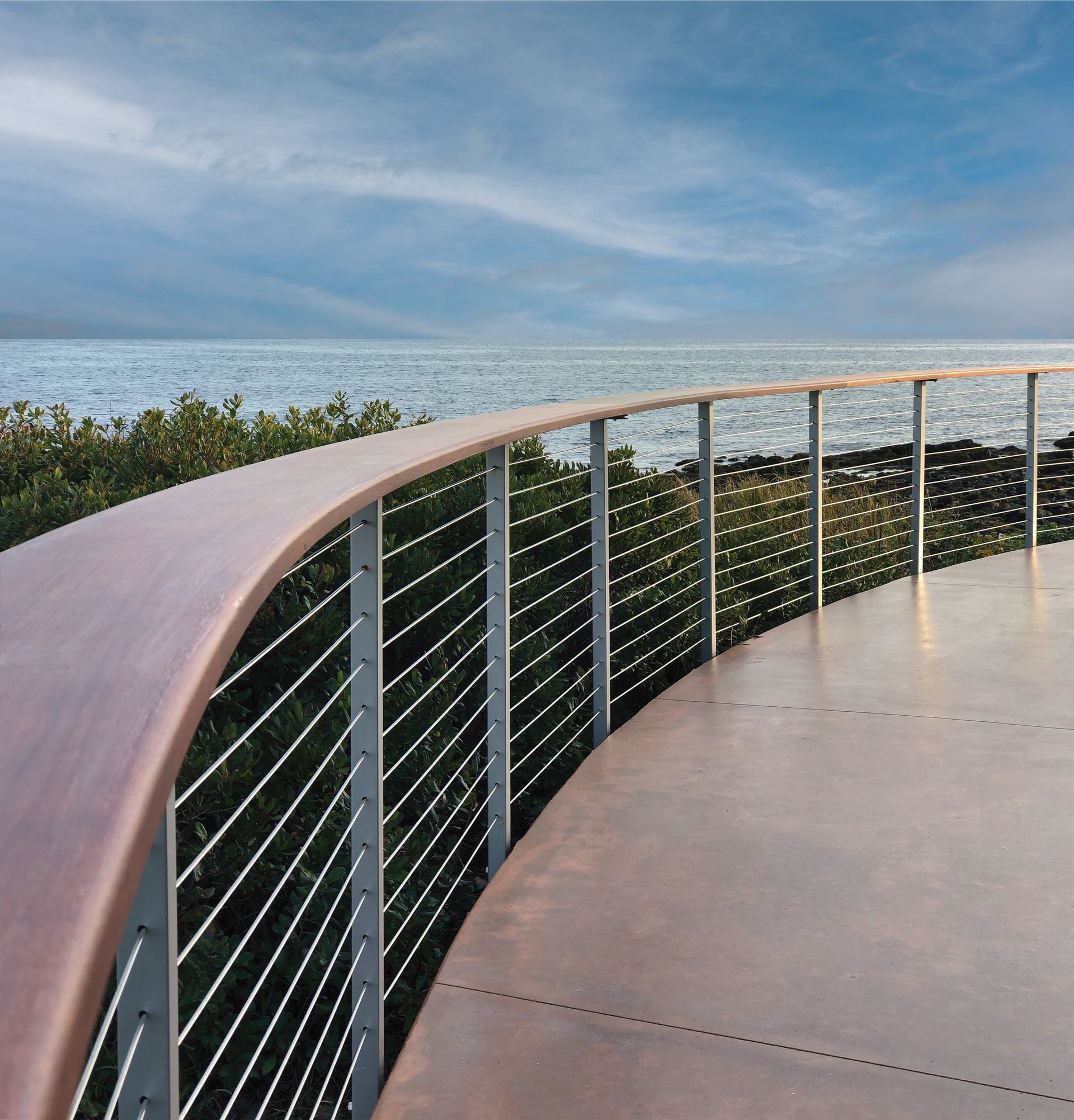 Curved seaside walkway with metal railing overlooking the ocean under a blue sky
