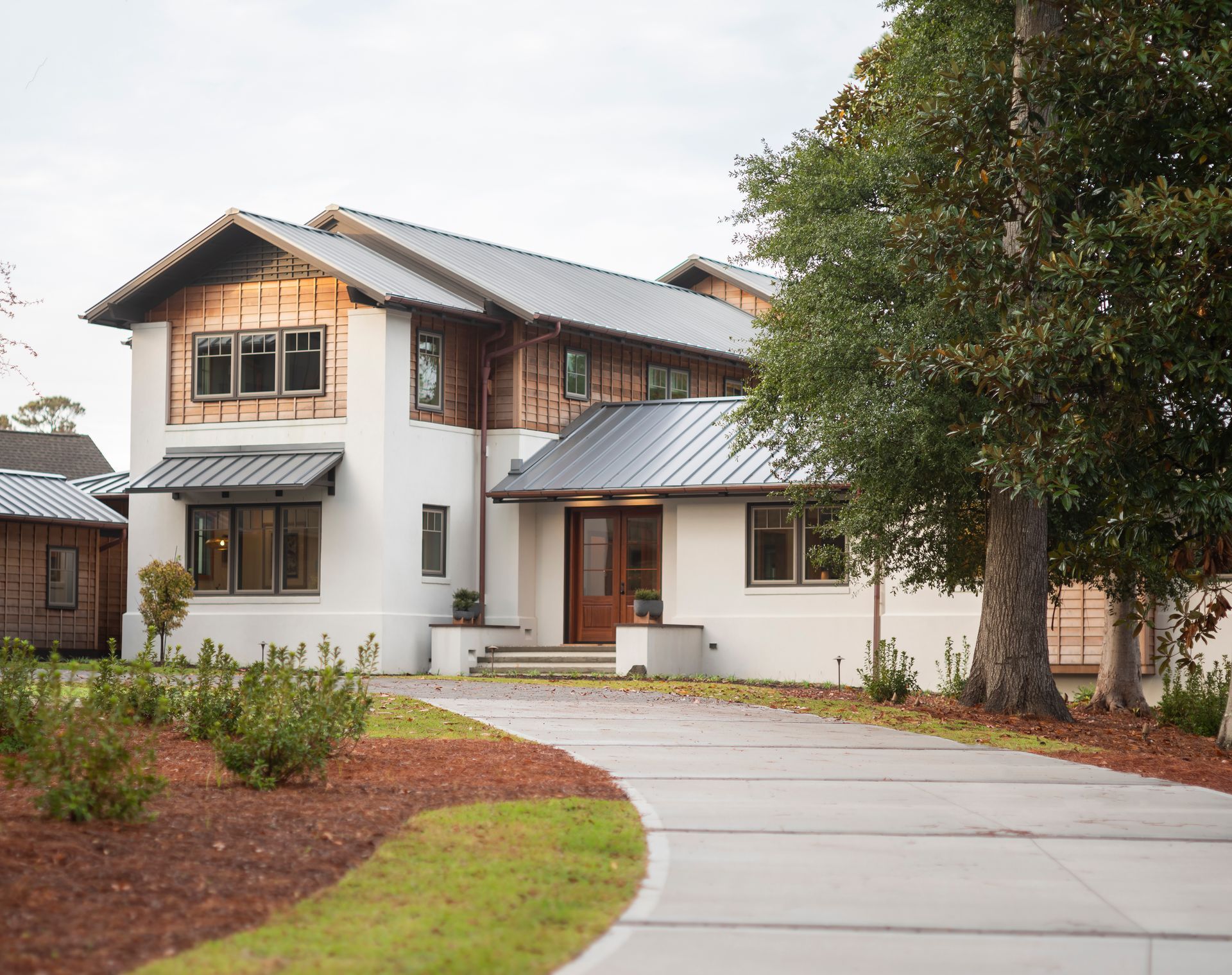 Modern two-story house with white walls, wood accents, and a curved driveway under a large tree
