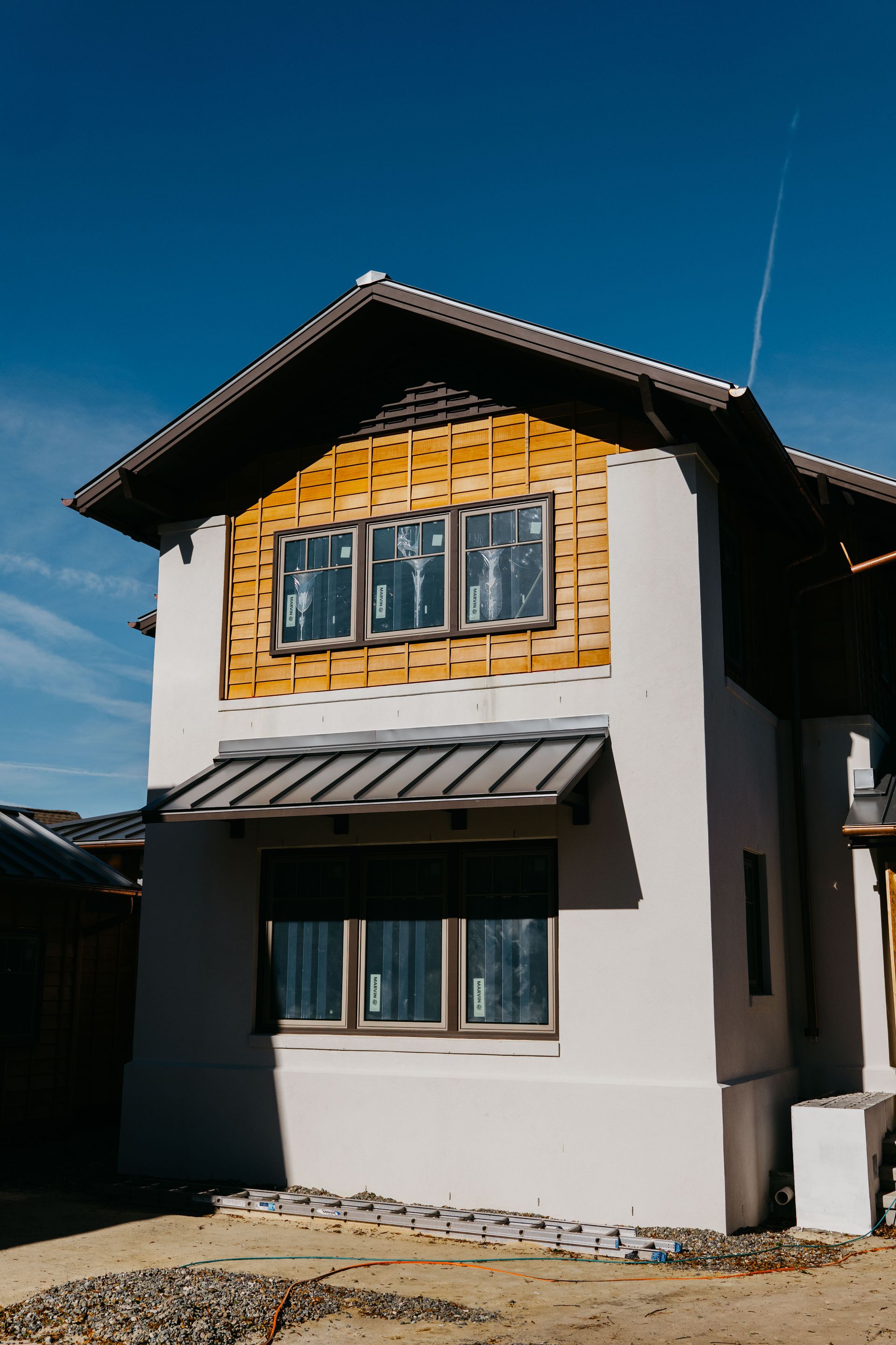 Two-story house with white walls, wooden balcony, and blue-gray window shutters under a clear blue sky