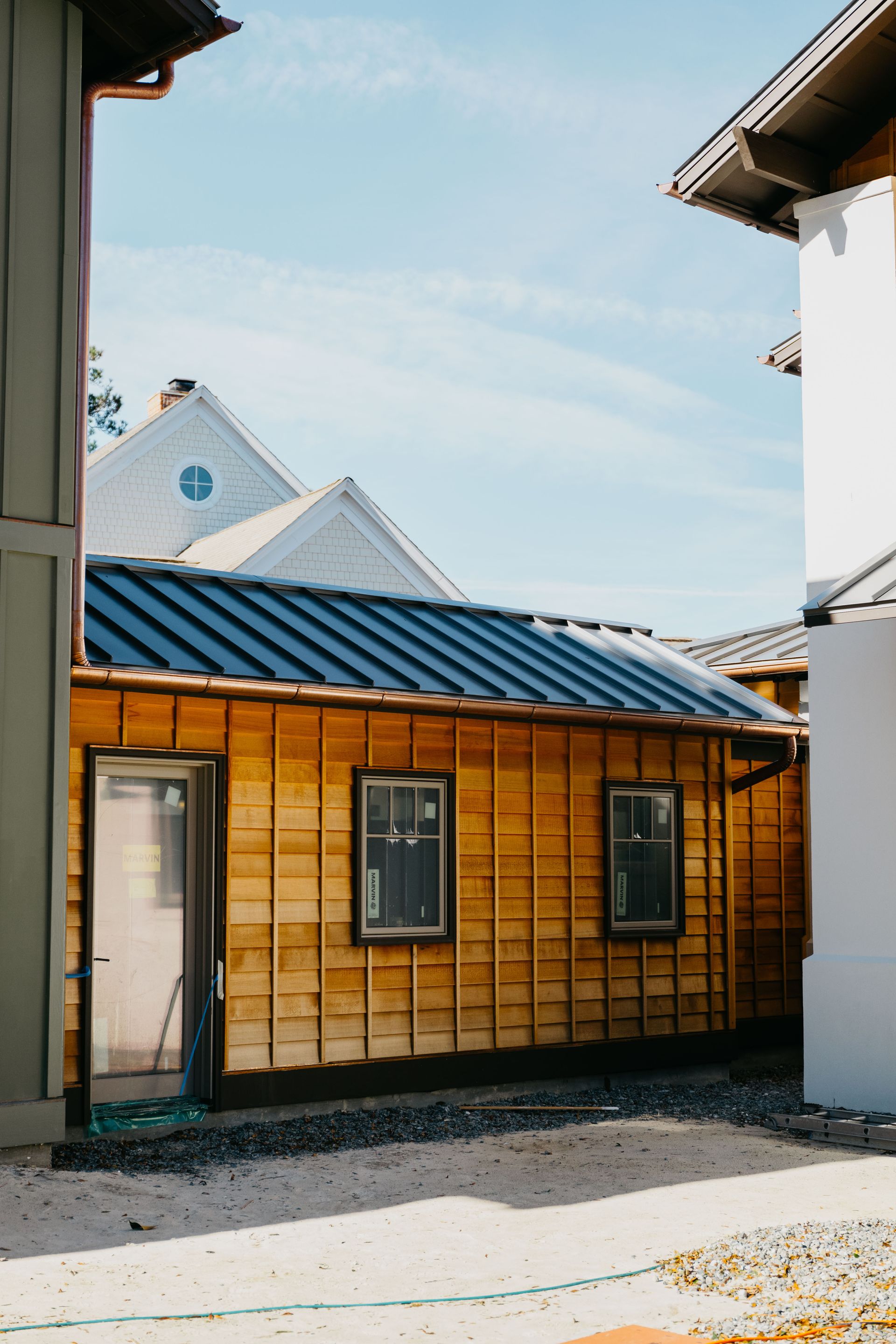 Narrow street view of a small wooden building with a blue metal roof between white walls under a clear sky
