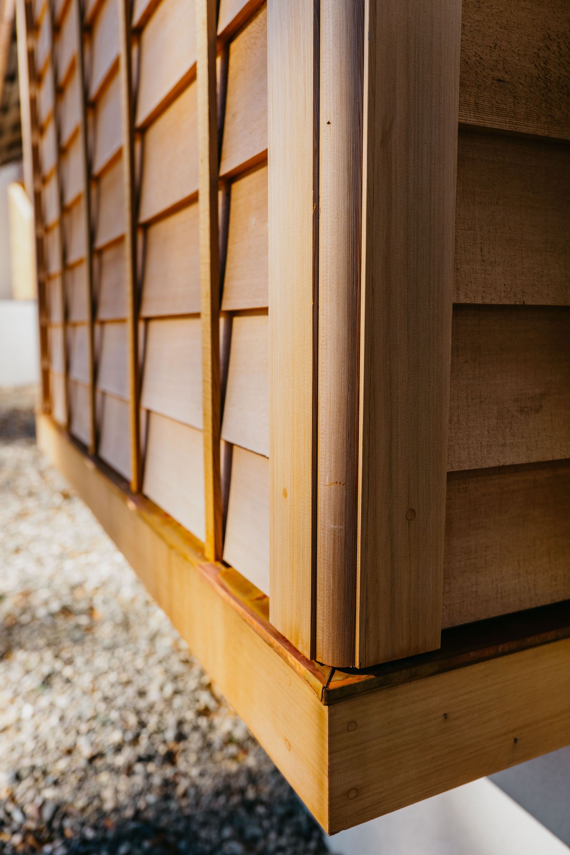 Wooden building corner with lattice siding and raised base on gravel