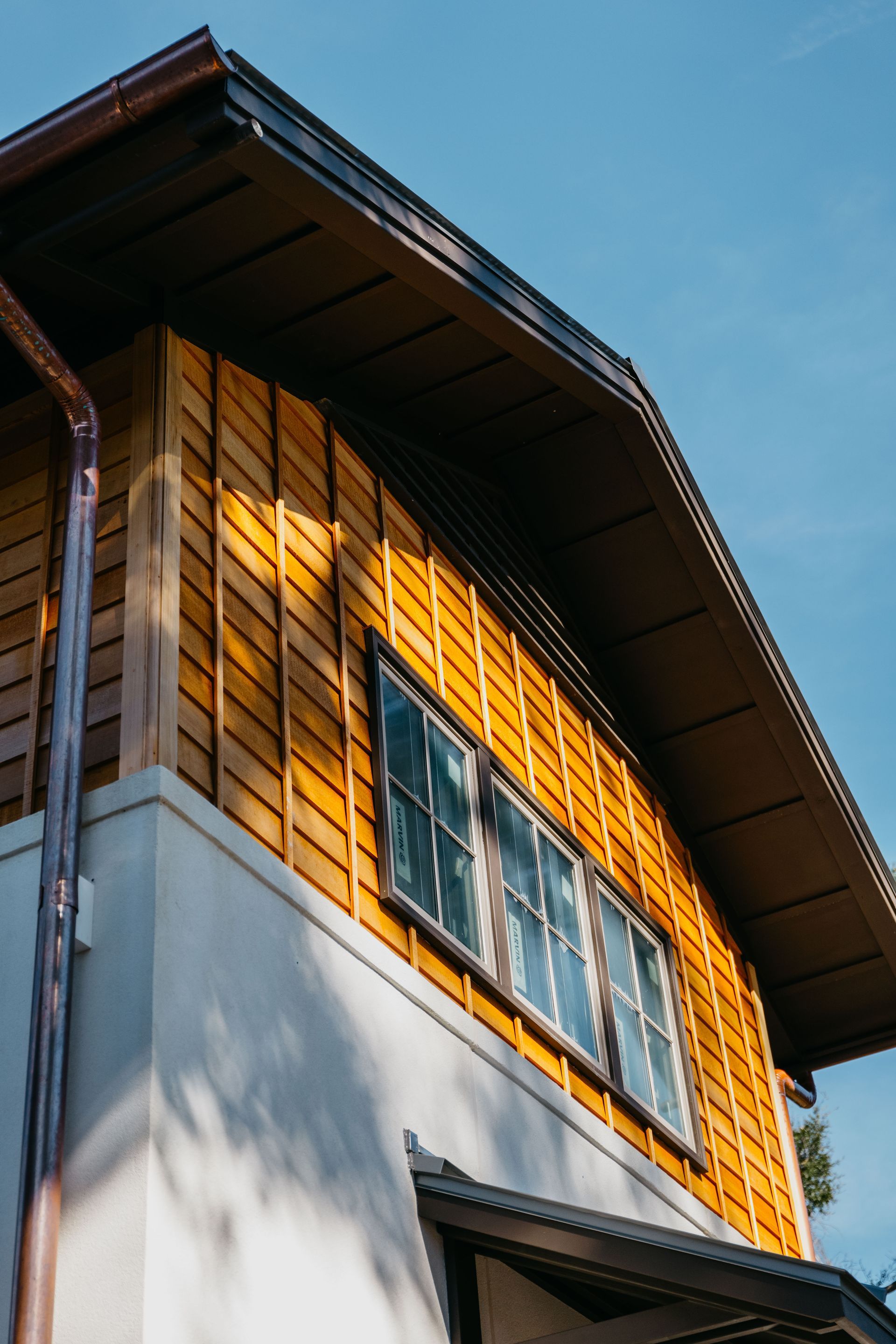 Sunlit wooden house exterior with large window and blue sky