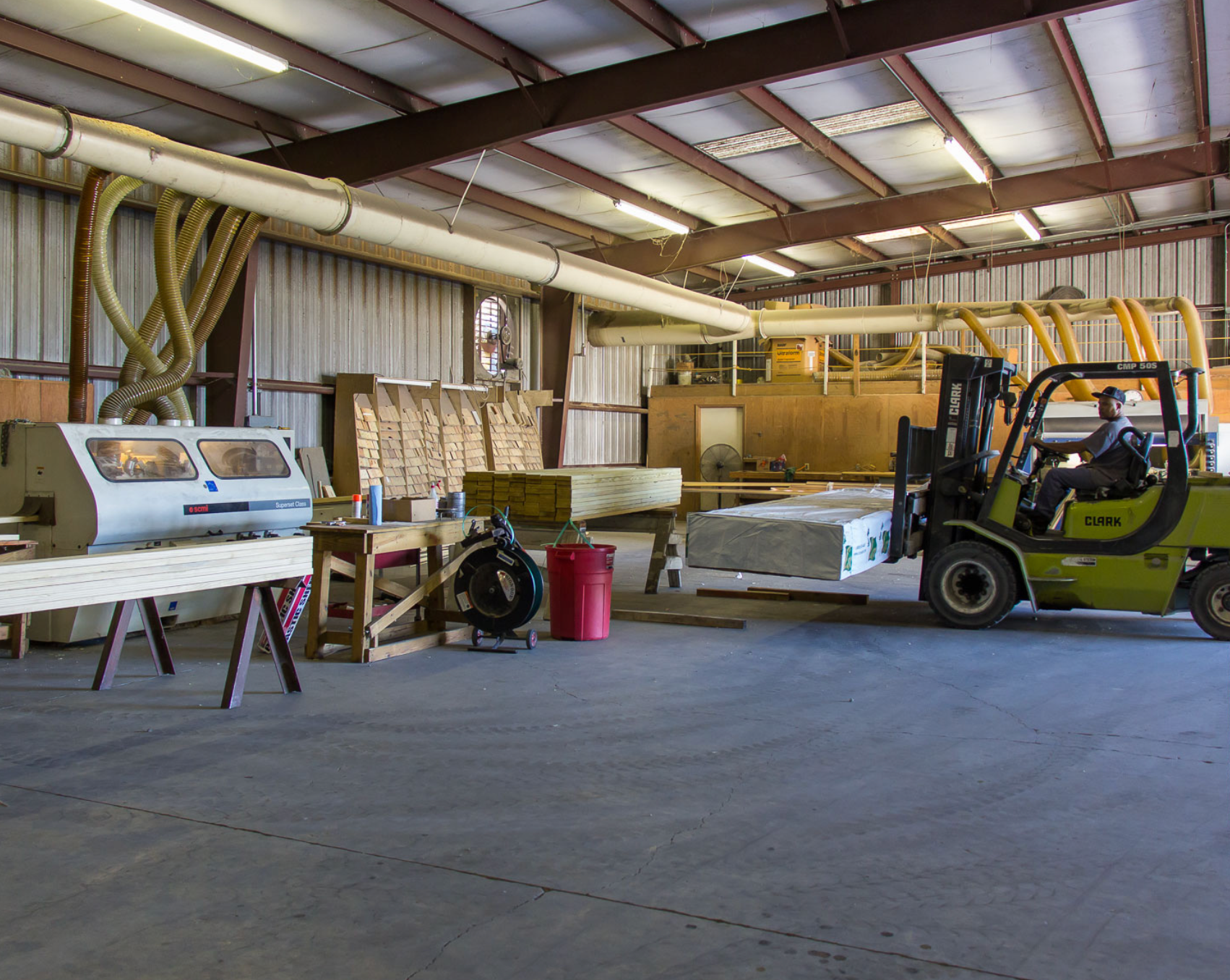 Warehouse interior with forklift, stacked wood, and industrial equipment