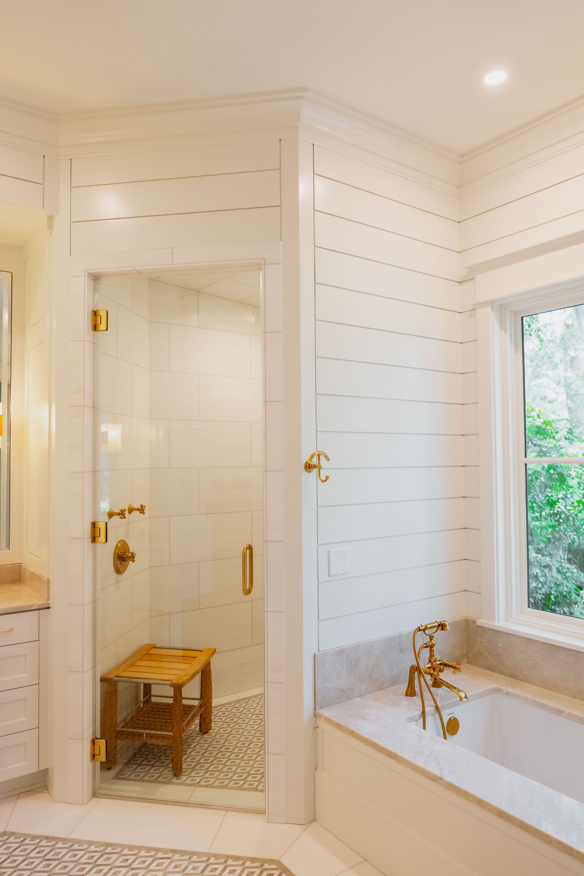 Bright bathroom with white shiplap walls, glass shower, and a freestanding tub by a window.