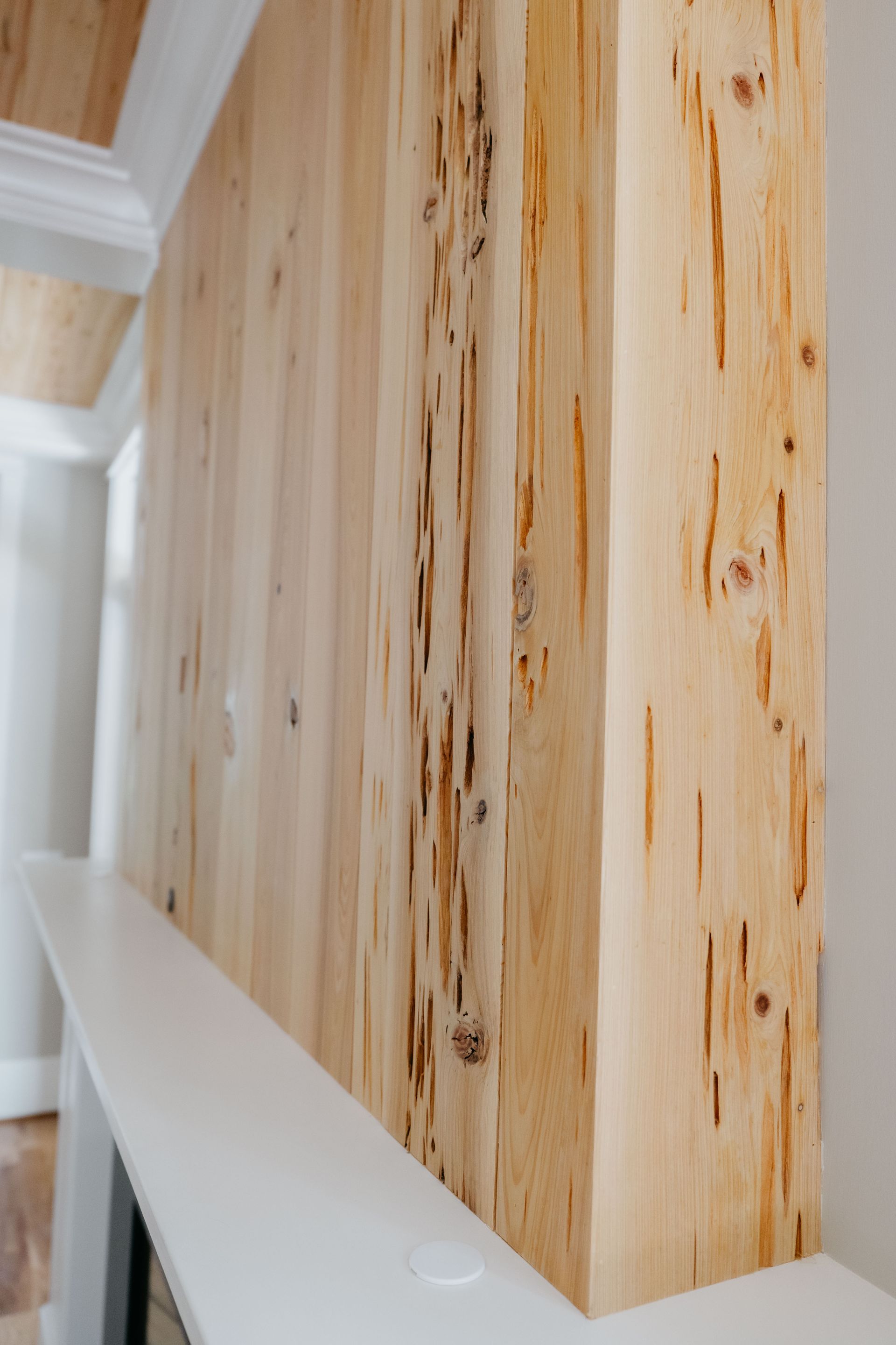 Close-up of light wood wall panels with dark knots and a white stair rail in a bright hallway