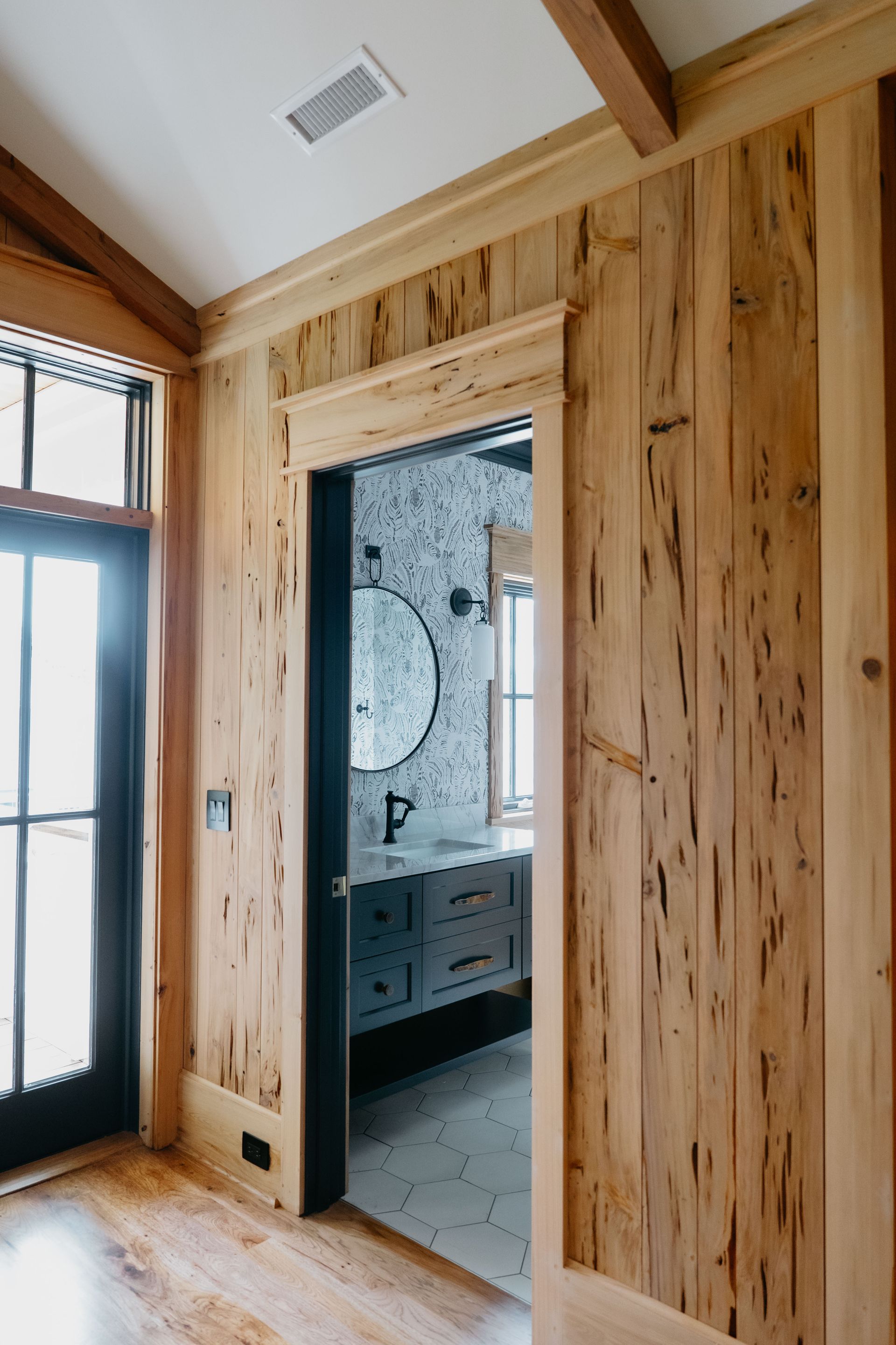 Wood-paneled hallway opening into a bathroom with a patterned tile wall and vanity sink