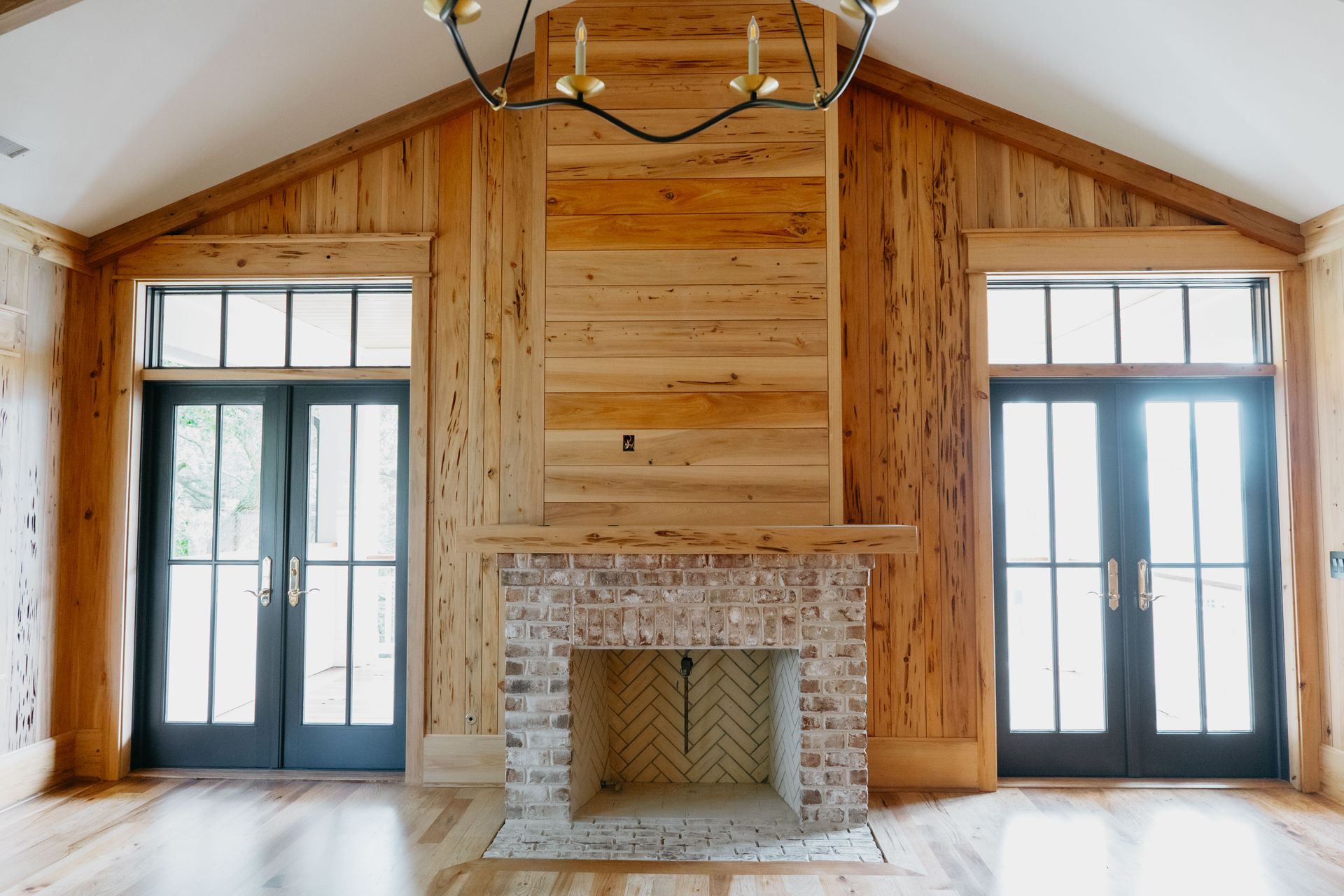 Wood-paneled living room with a brick fireplace and tall windows on either side