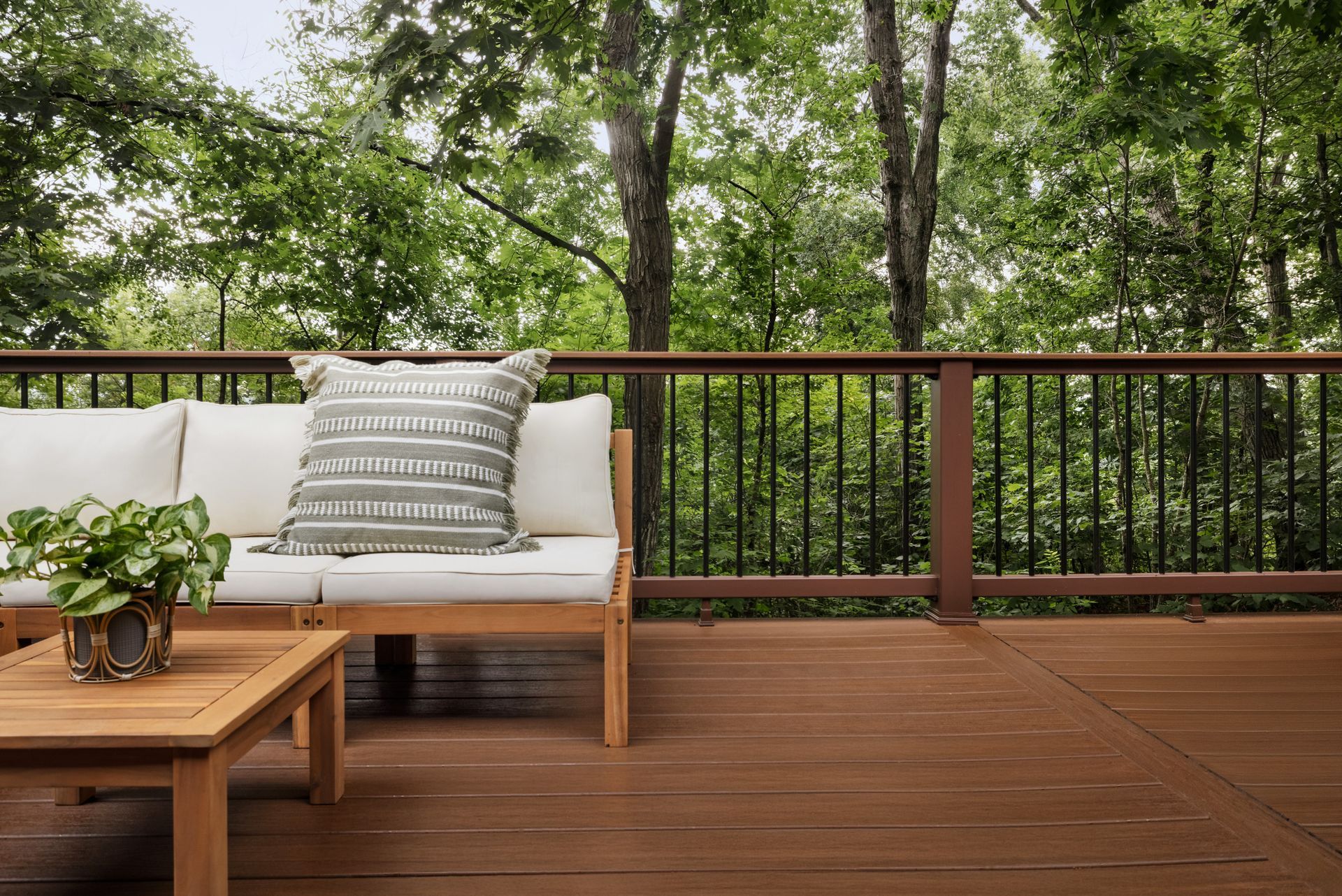 Wooden deck with cushioned chair, coffee table, and forest view beyond railing