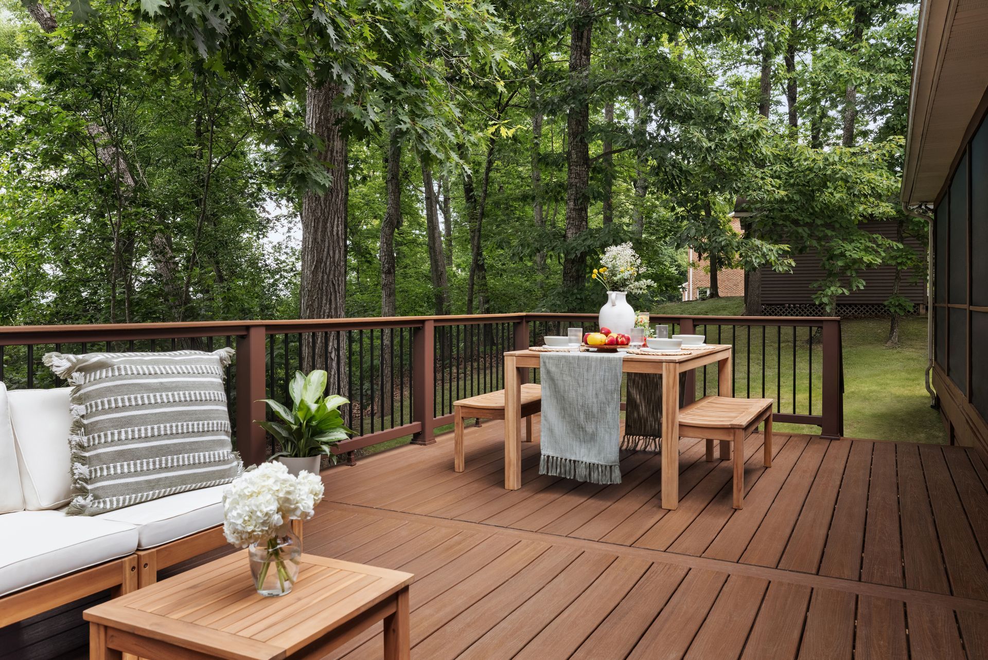 Wooden deck with outdoor dining table, benches, and cushioned chair in a wooded backyard