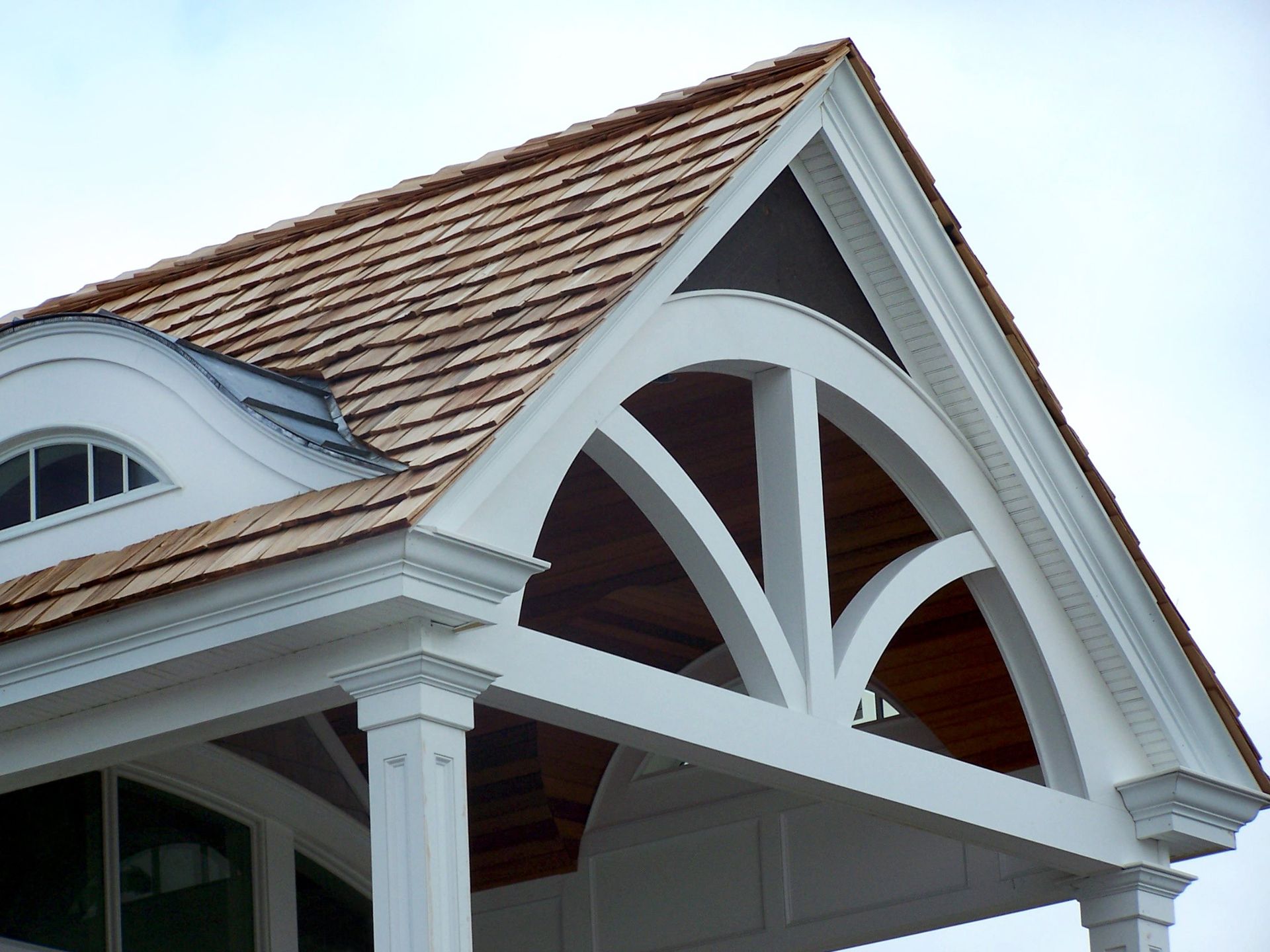 White house gable with decorative arched trim and brown shingled roof against the sky
