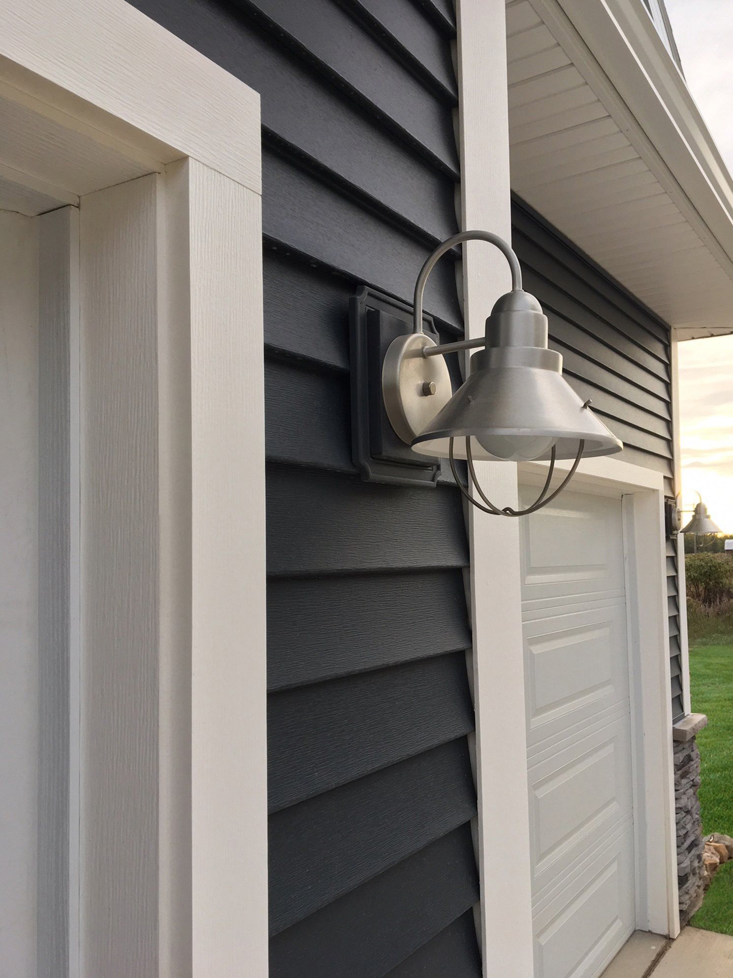 Exterior wall-mounted porch light beside a garage, with dark gray siding and white trim.