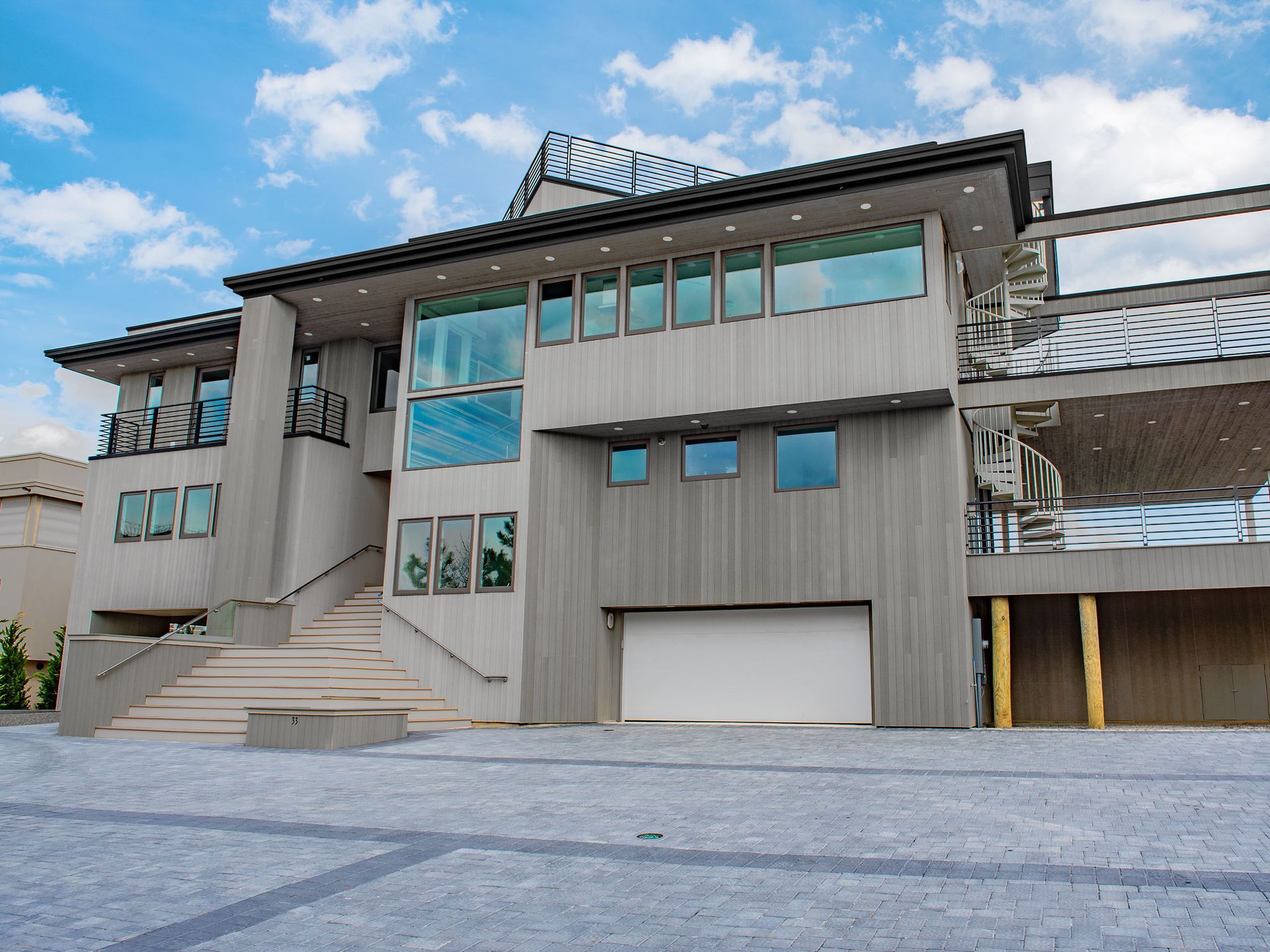 Modern gray two-story house with large windows and a garage under a blue sky