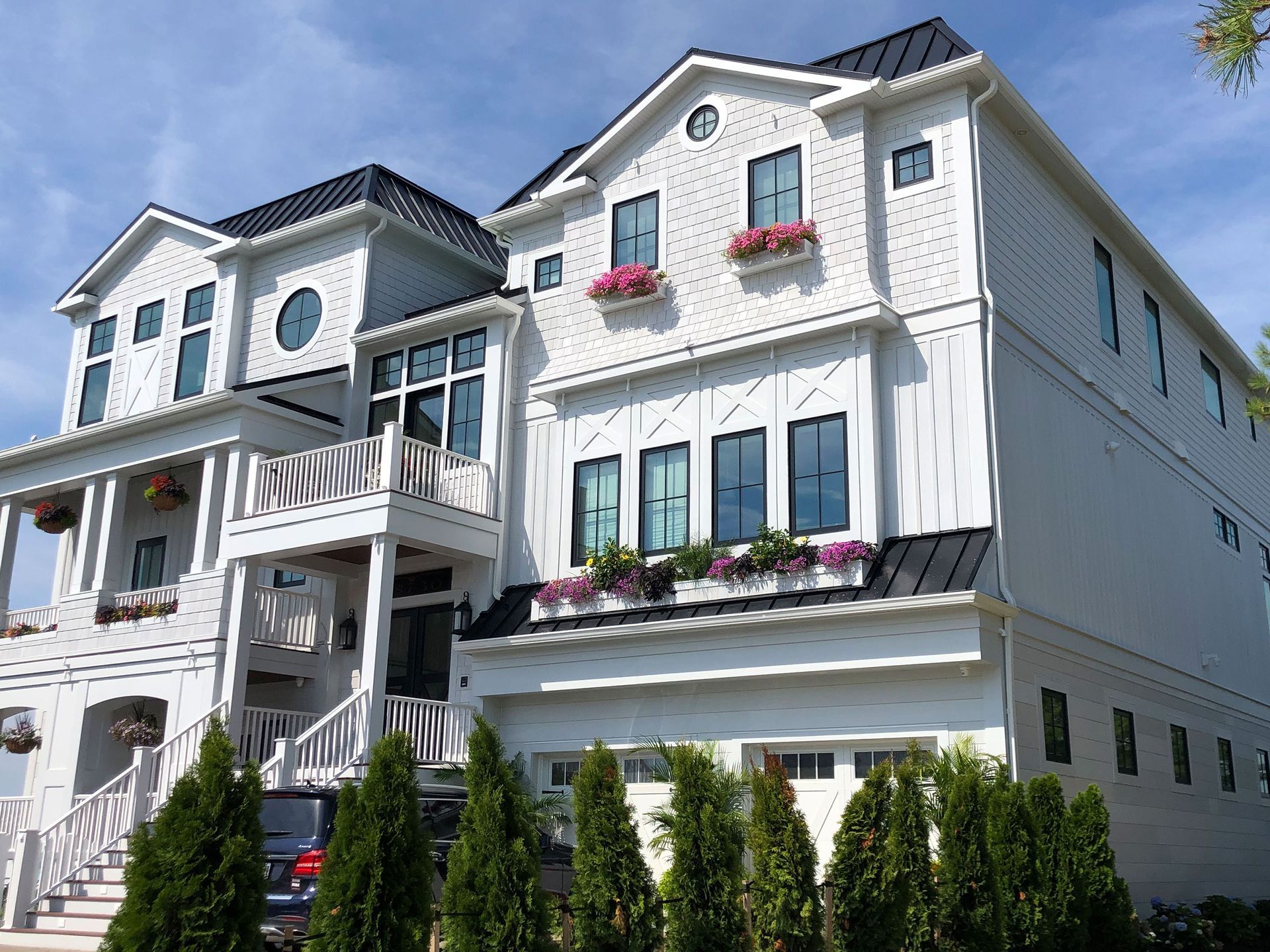 White multi-story townhouse with balconies, flower boxes, and tall shrubs under a blue sky