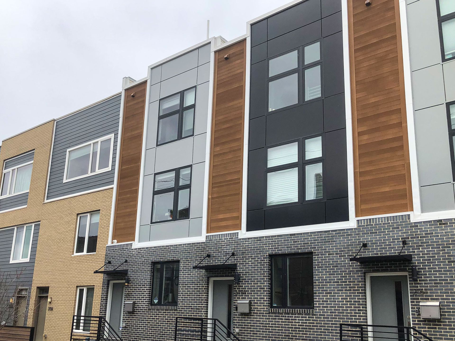 Modern row houses with gray, black, and wood facades along a street under an overcast sky