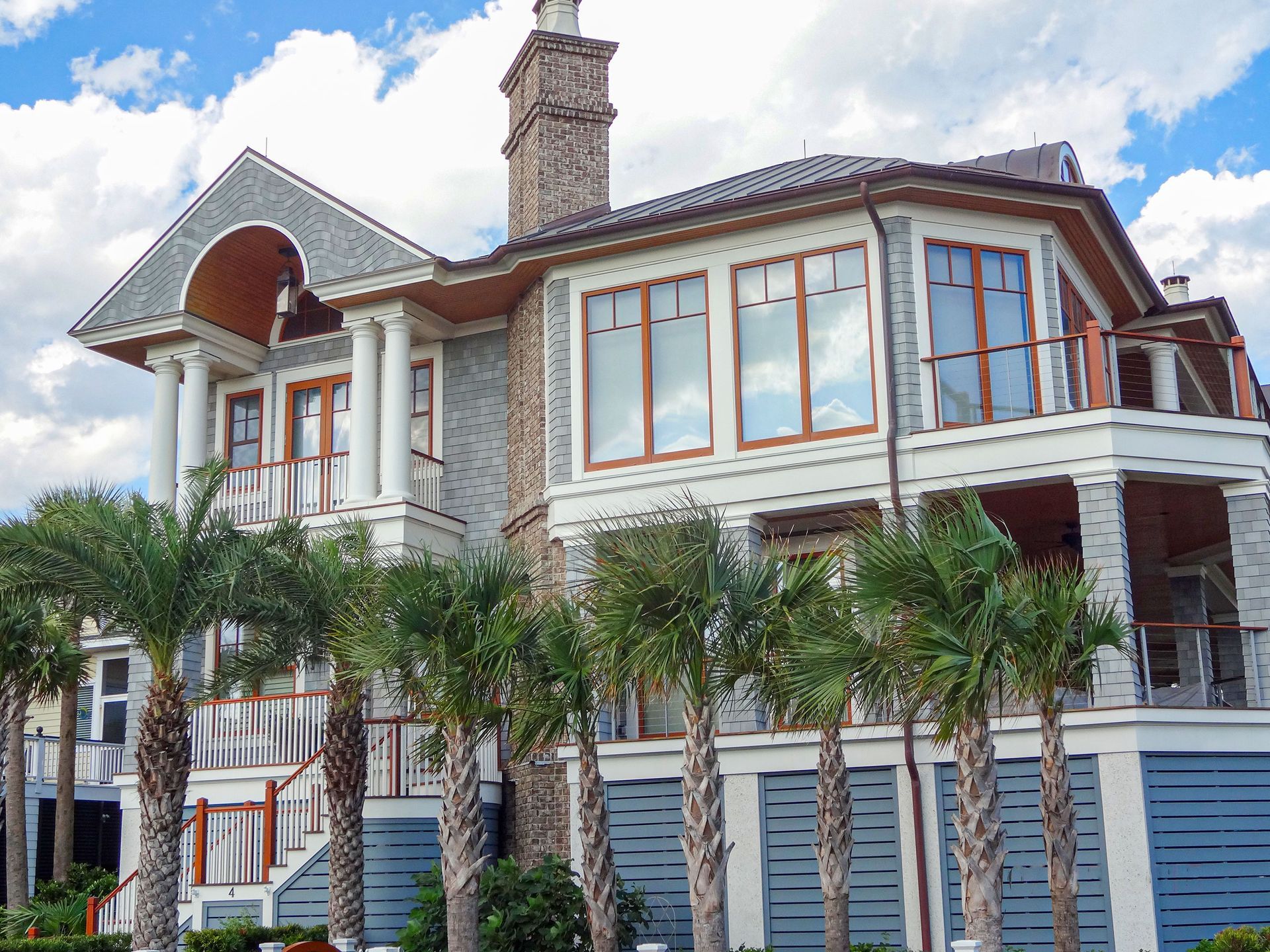 Large white stone house with blue trim, arched balcony, and palm trees in front