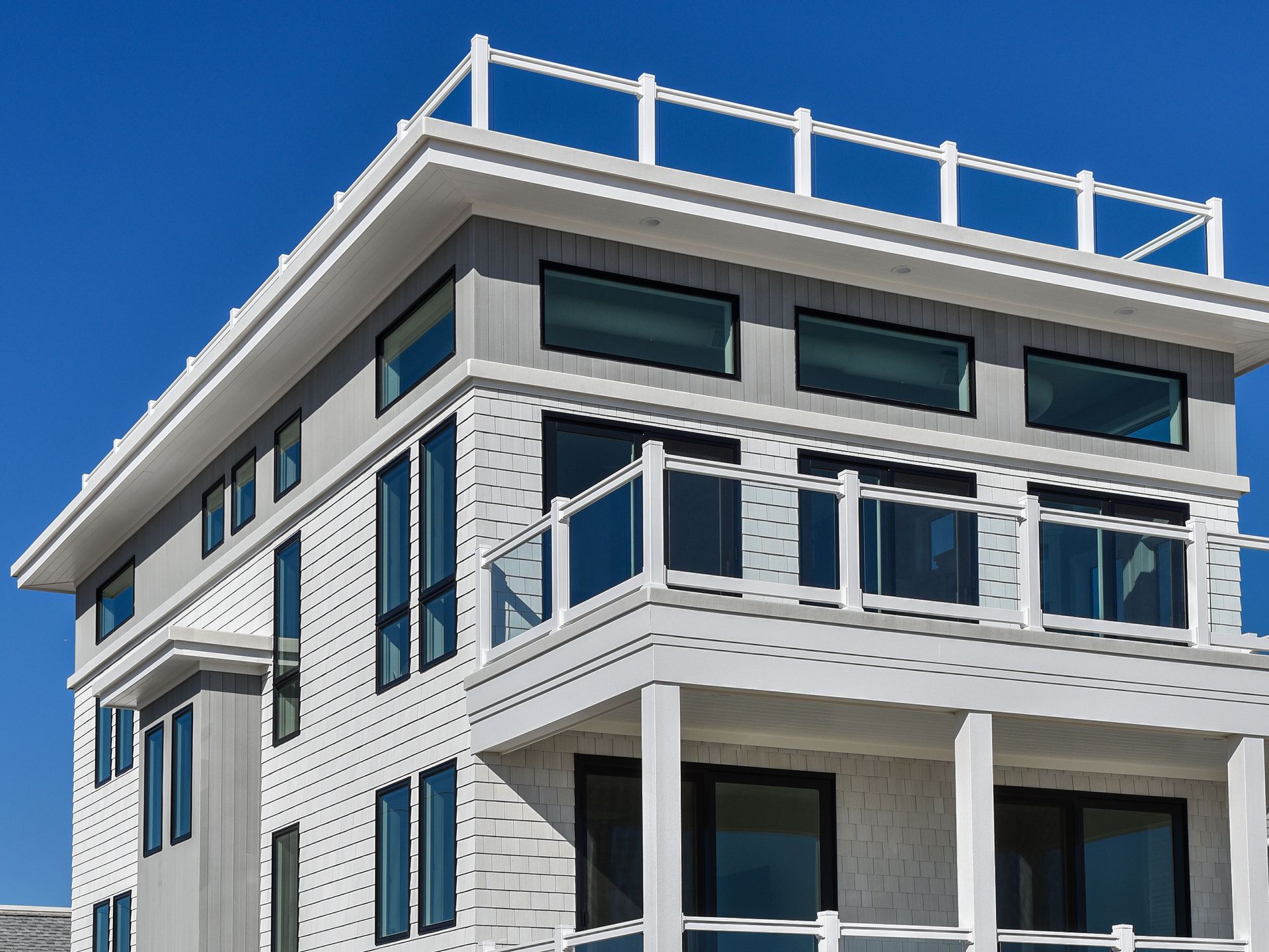 Modern white multi-story house with blue-gray trim and balconies against a clear blue sky