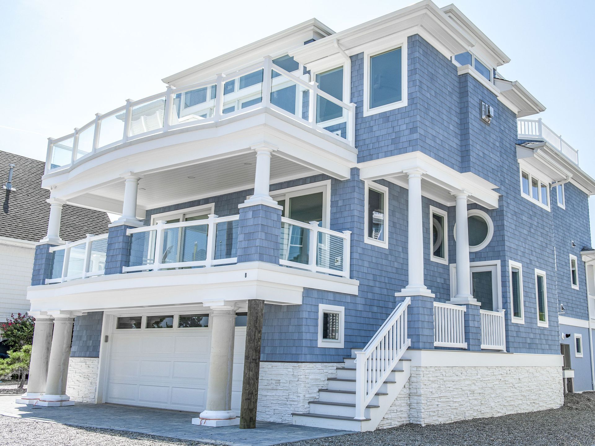 Blue seaside house with white trim, balconies, and a garage under a bright sky