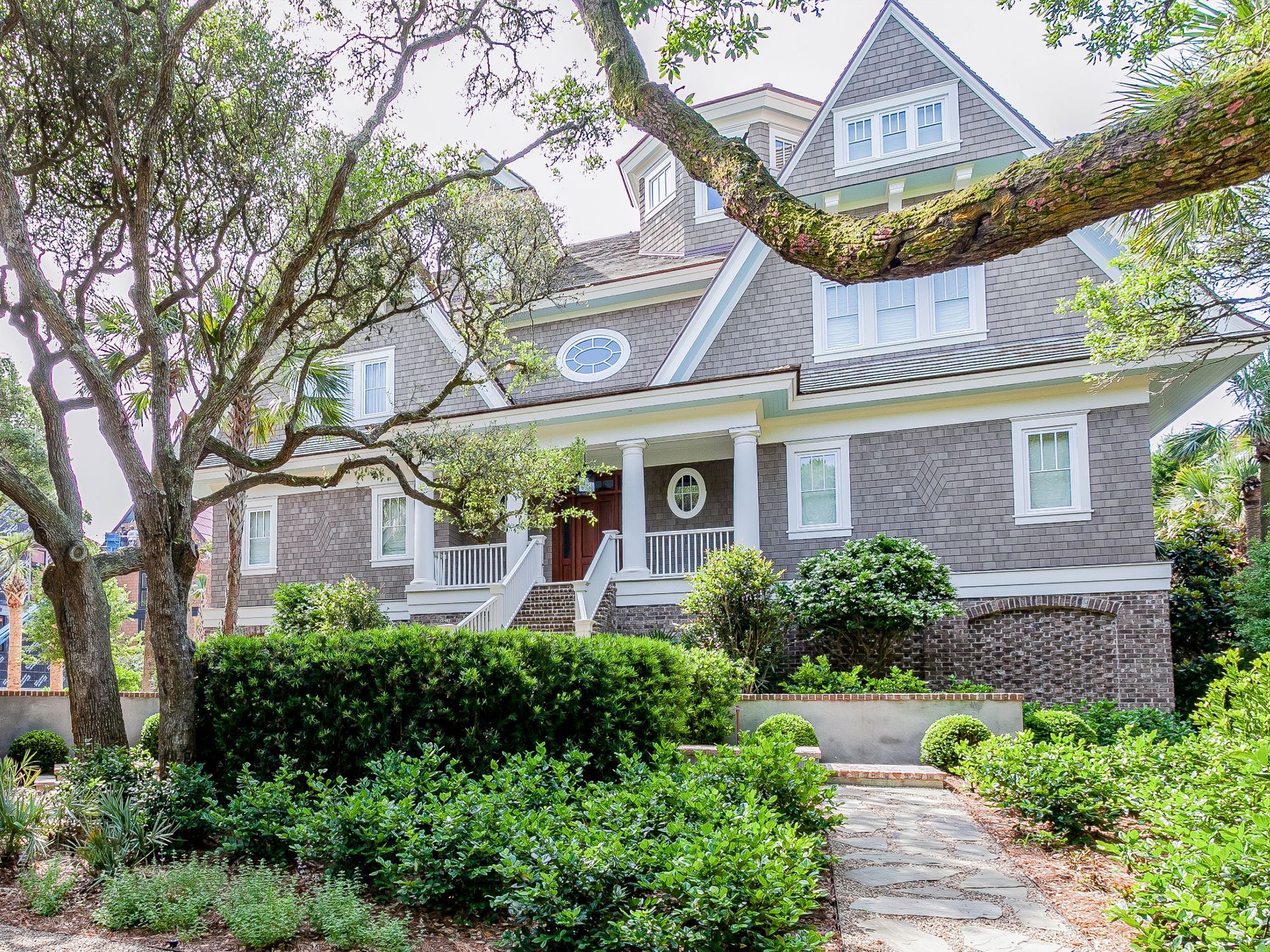 Stone house with a front porch, gabled roof, and lush green garden along a brick walkway.