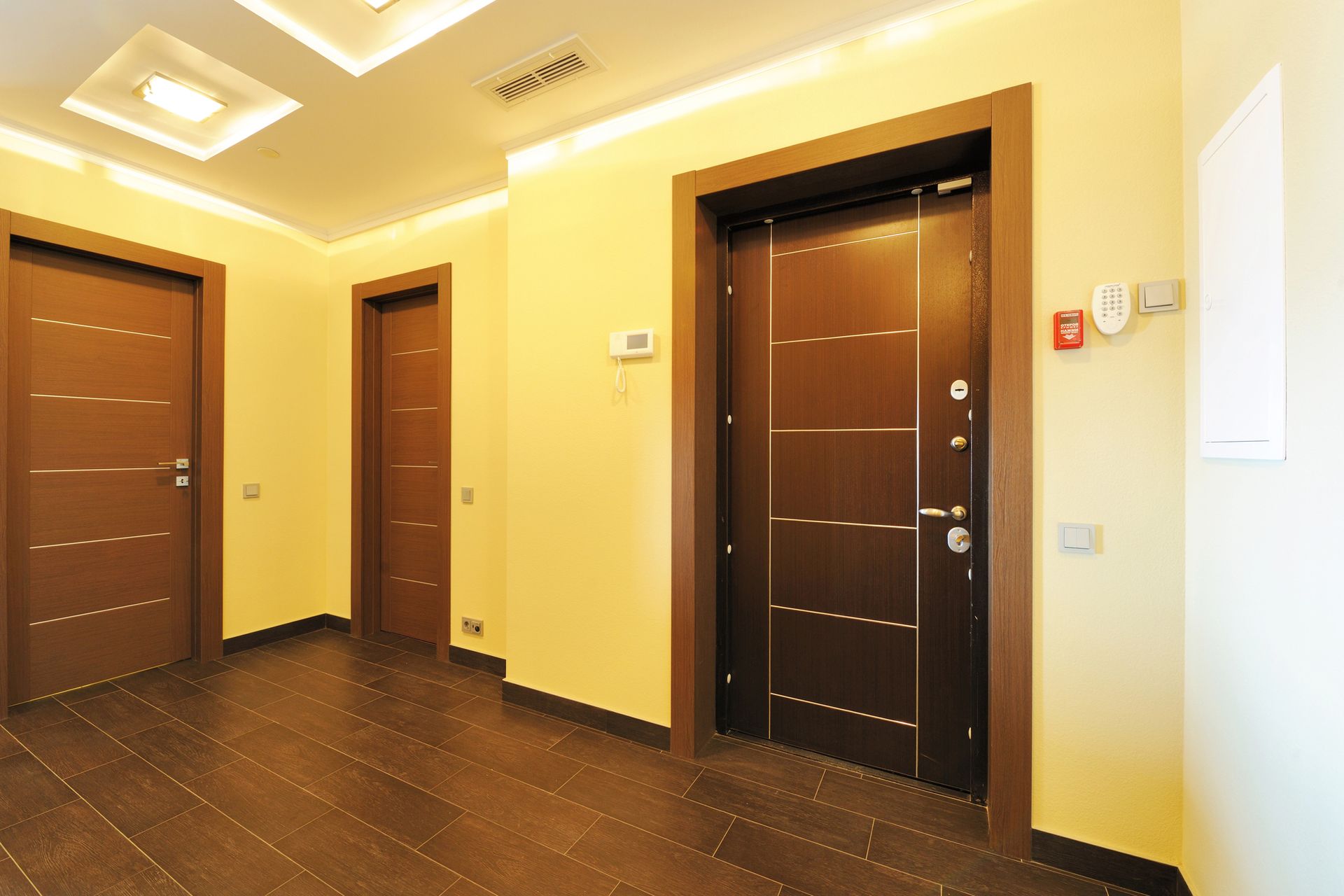 Corridoio di un appartamento moderno con porte marrone scuro e illuminazione giallo caldo.