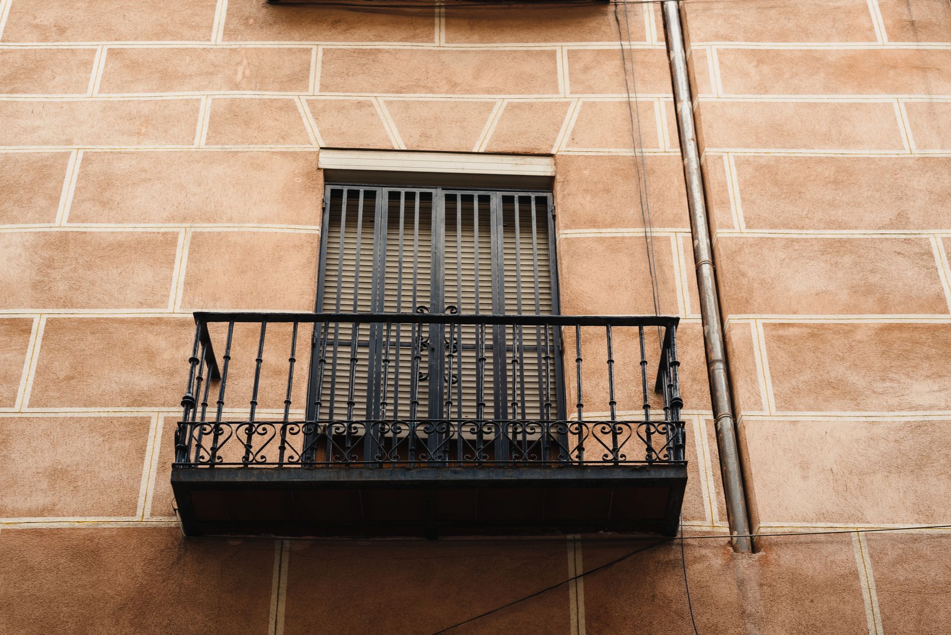 Piccolo balcone nero su un edificio in mattoni con finestra chiusa e ringhiera in metallo.