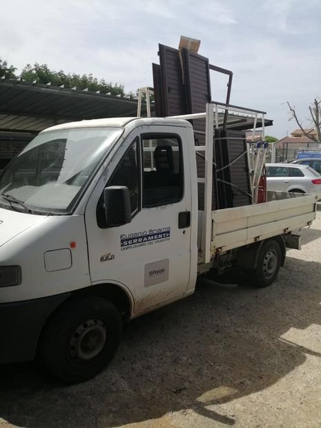 Un camioncino bianco con pianale, carico di telai metallici impilati, parcheggiato in un'area di sosta.