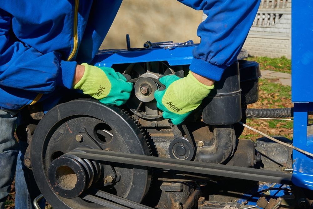A Person in a Blue Jacket and Bright Green Work Gloves Adjusts a Belt and Pulley — Aspire Diesel In Dingo, QLD