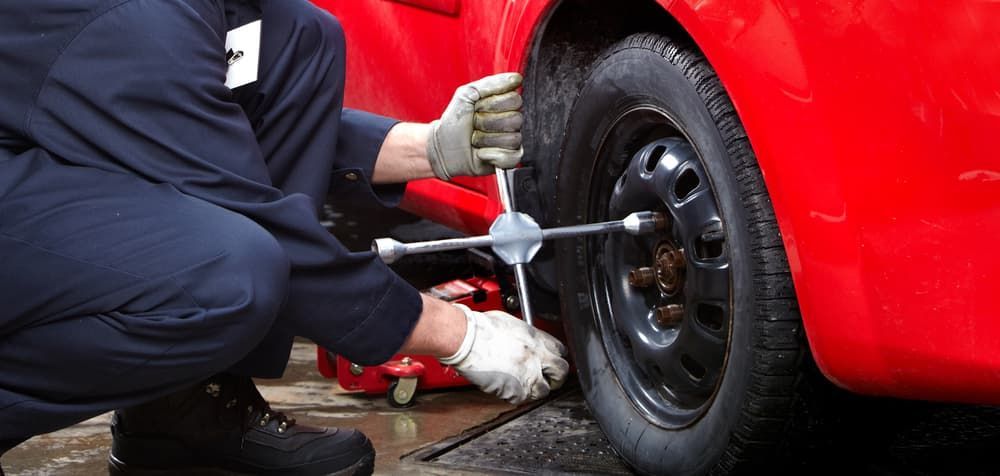A Man is Changing a Tire on a Red Car With a Wrench — Aspire Diesel In Dingo, QLD