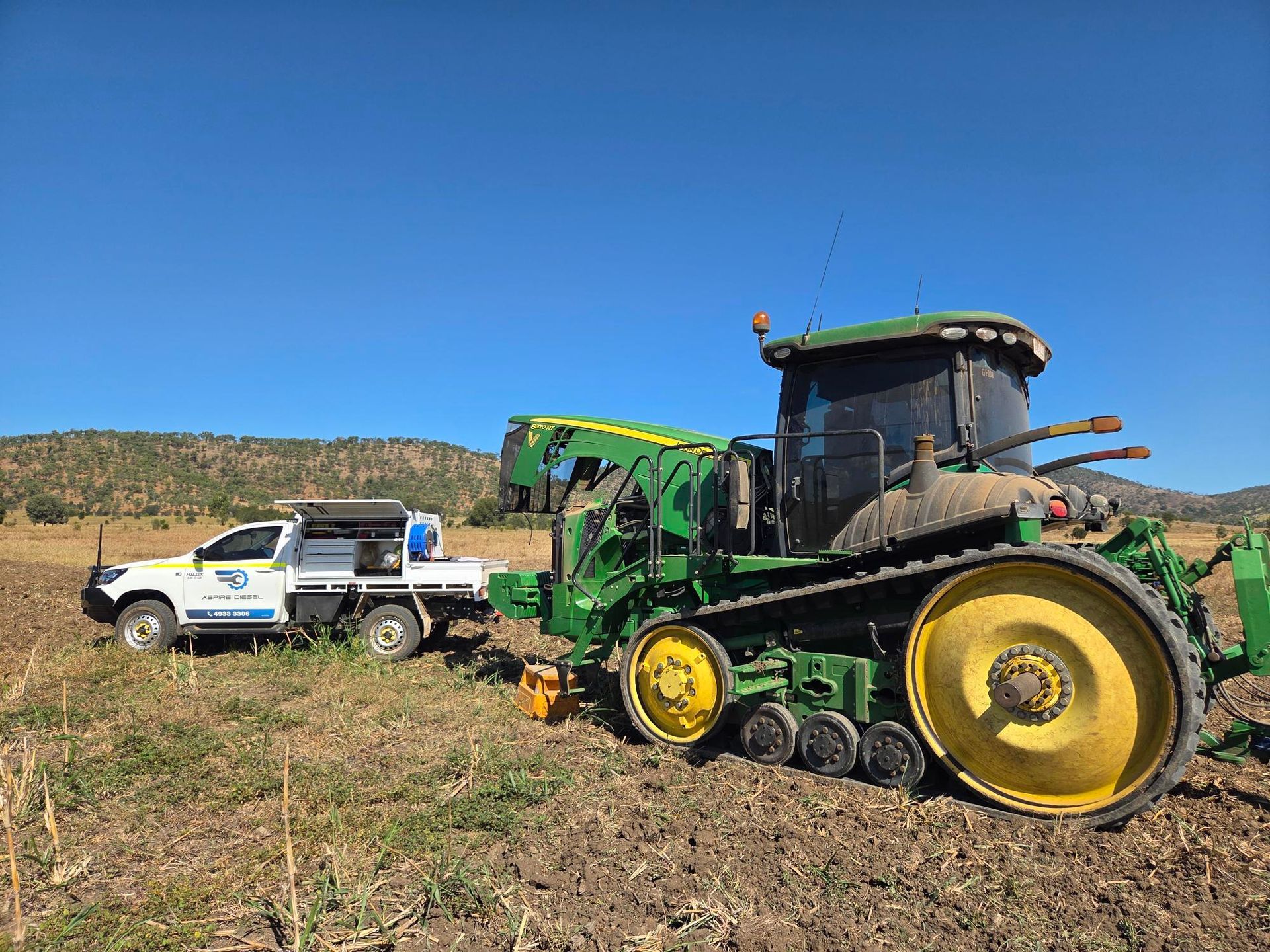 Green John Deere combine harvester beside a white pickup in a dry field under a blue sky - Aspire Diesel In Gracemere, QLD