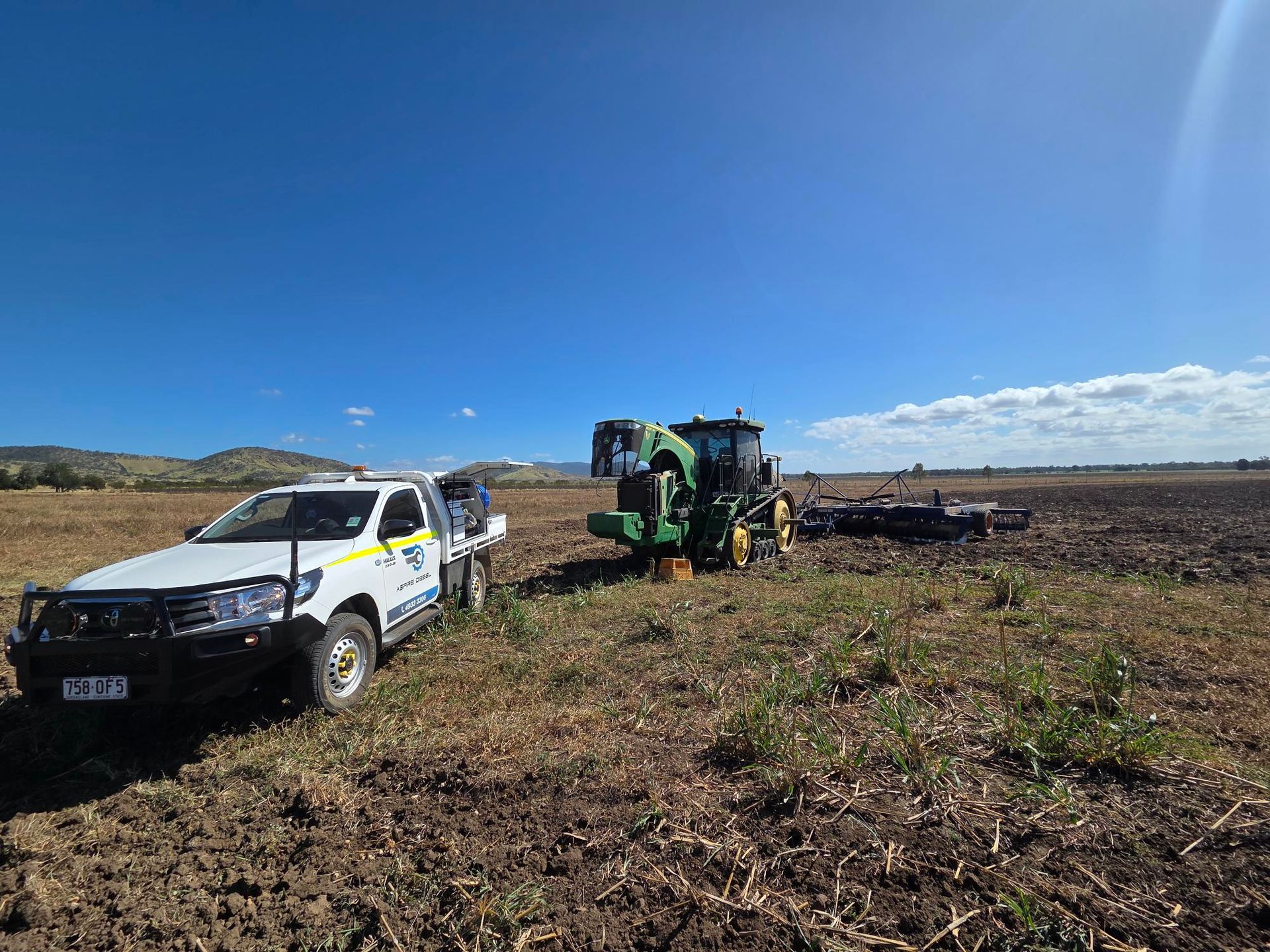 White utility truck and green tractor in a harvested field under a clear blue sky - Aspire Diesel In Gracemere, QLD