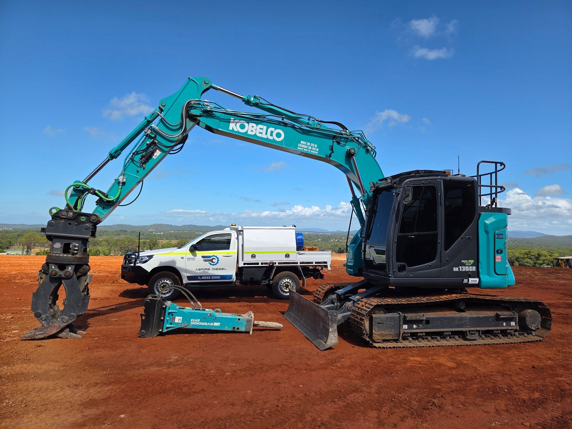 Turquoise excavator loading dirt beside a white utility truck on a red dirt construction site under blue sky — Aspire Diesel In Gracemere, QLD