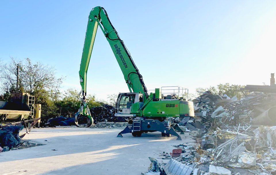 A large green crane is sitting in a pile of scrap metal.